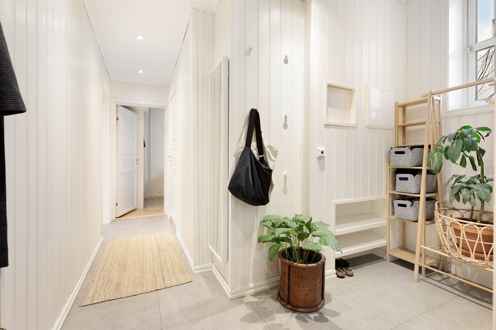 Gangen er romslig med god plass til oppbevaringsløsninger for klær og sko. Flere praktiske hylleløsninger gjør det enkelt å henge fra seg. Lysmalte flater og delikate fliser med underliggende gulvvarme gir en lun og hyggelig velkomst. Galleribilde