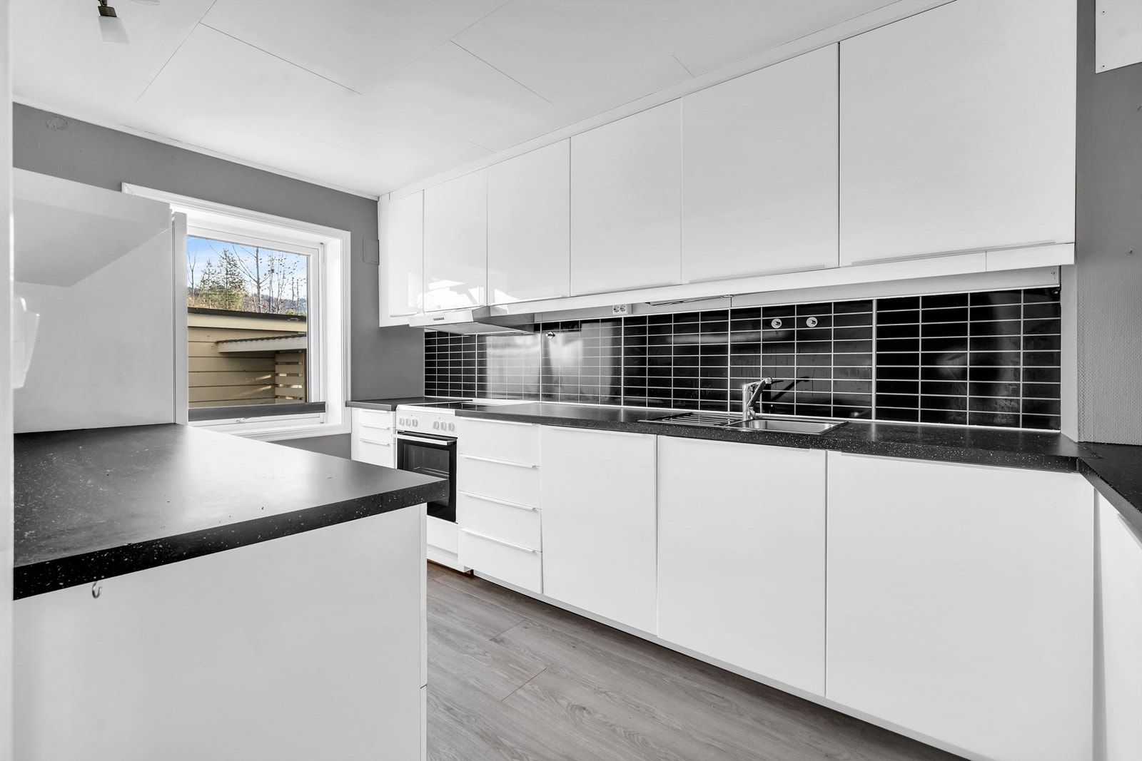 Kjøkken med antatt Ikea innredning i hvit høyglans med takhøye overskap. Det er benkeplate i laminat med sponkjerne. Galleribilde