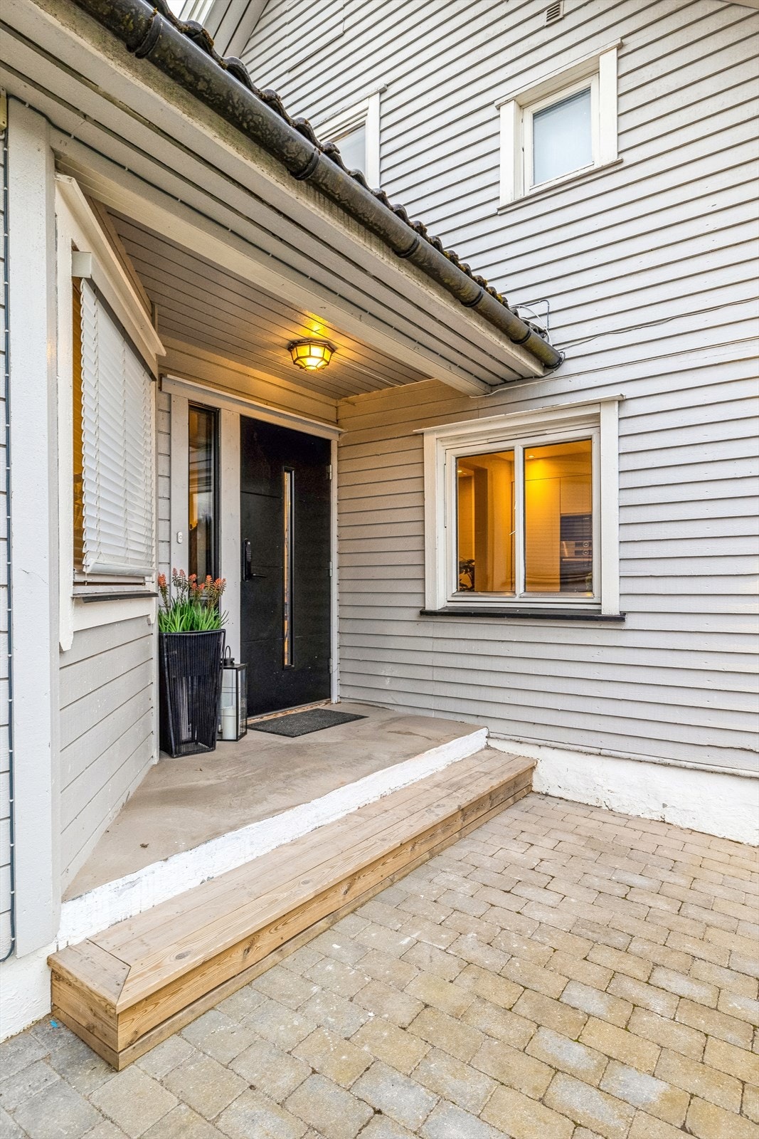 Inngangsparti med overbygg, ny dør (2024). Steinlagt gårdsplass med god plass til biloppstillingsplasser. Galleribilde