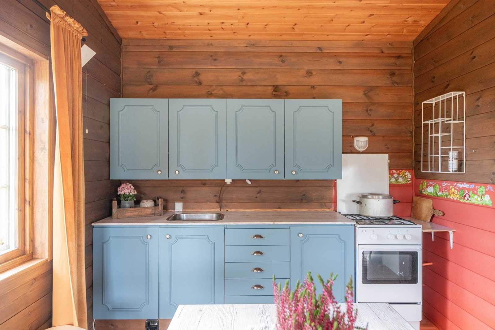 Kjøkkendelen har en enkel innredning fra byggeår med profilerte fronter. Det er lagt opp vannslange, pumpe og kran til underskap hvor det kan pumpes vann fra nærliggende bekk. Selger har benyttet gasskomfyr og kjøleskap. Galleribilde