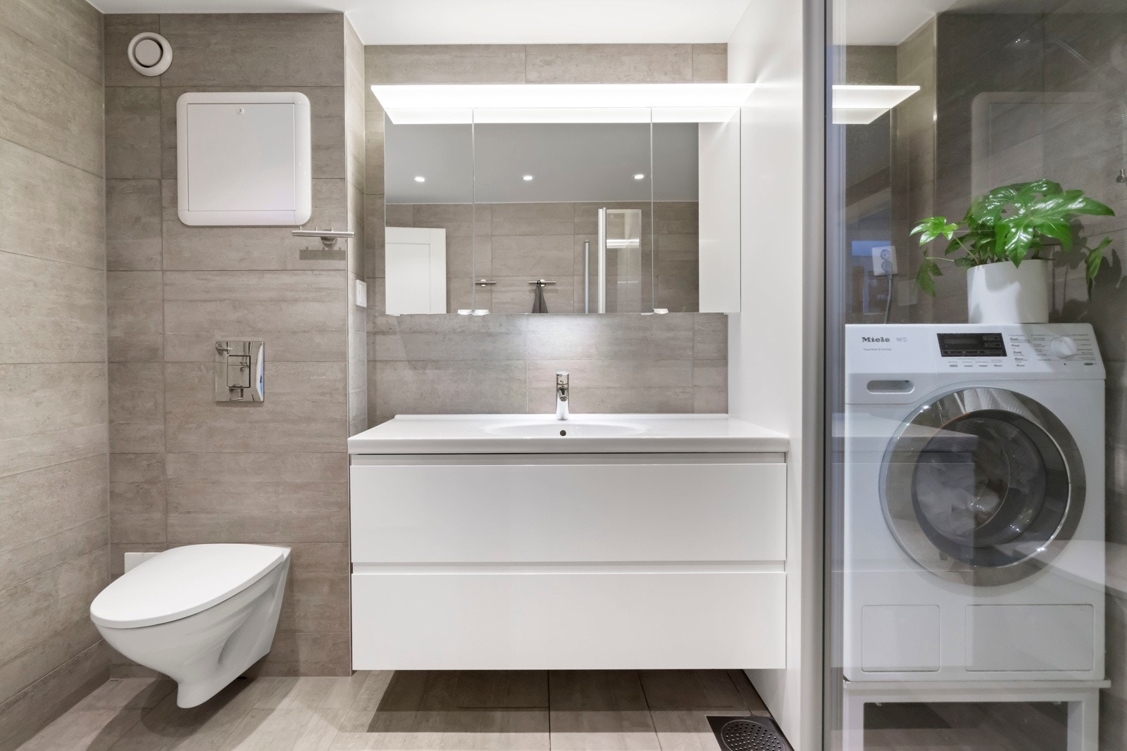 Badet har vegghengt wc og heldekkende servant og praktisk nisje for vaskemaskin og tørketrommel Galleribilde