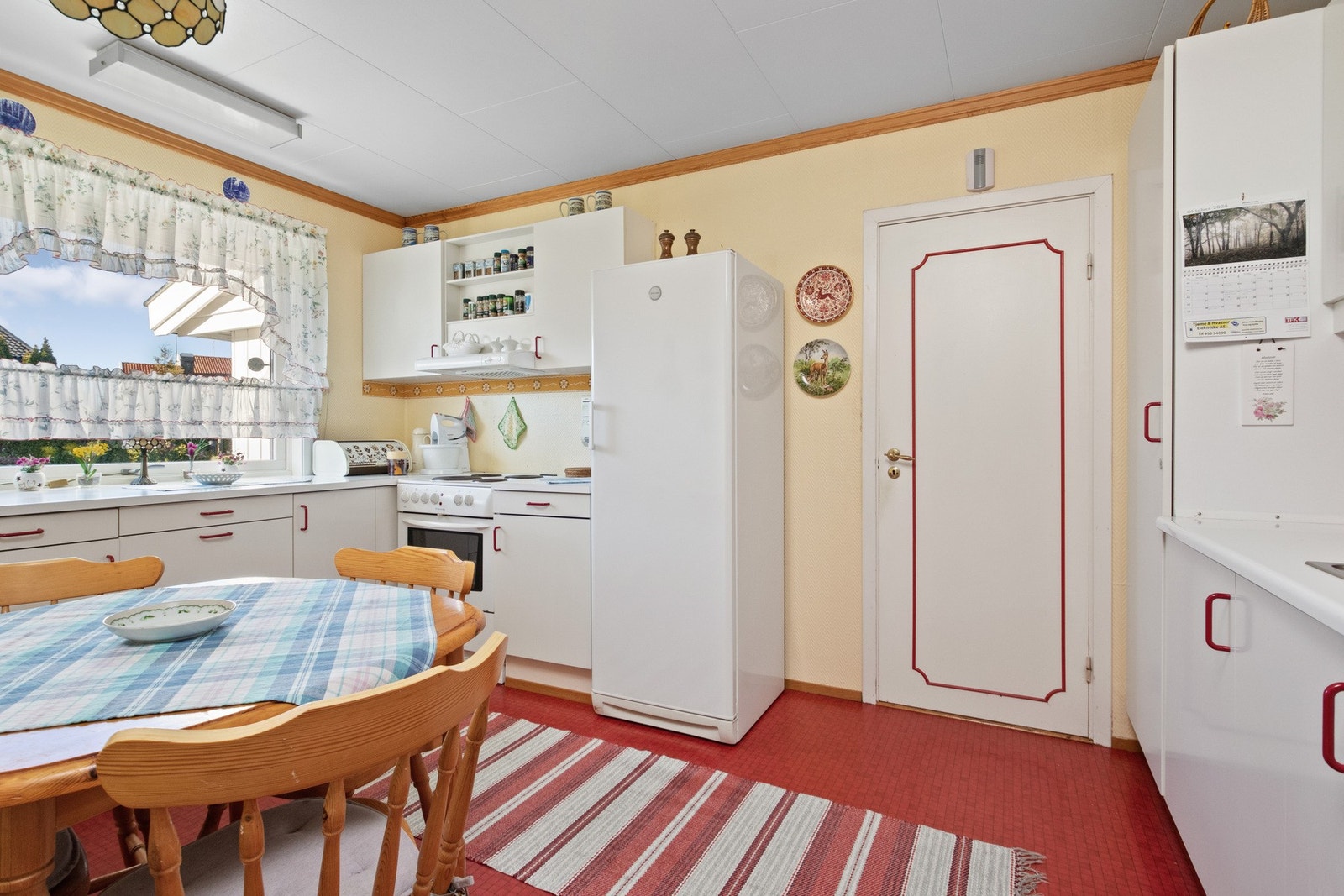 Kjøkkenet ligger innenfor stuen, med vinylbelegg på gulvet og lys tapet på veggene. Galleribilde