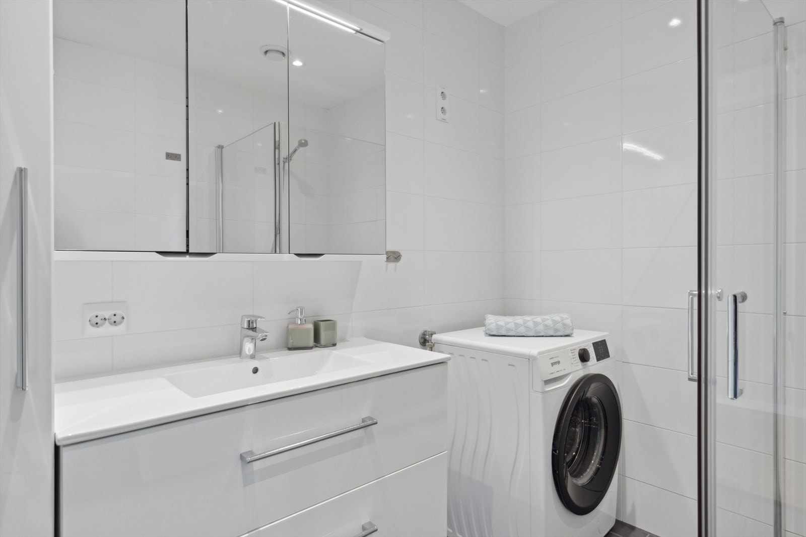 På badet er det dusjnisje med glassdører, toalett, baderomsinnredning, høyskap og speilskap.
Opplegg for vaskemaskin. Galleribilde