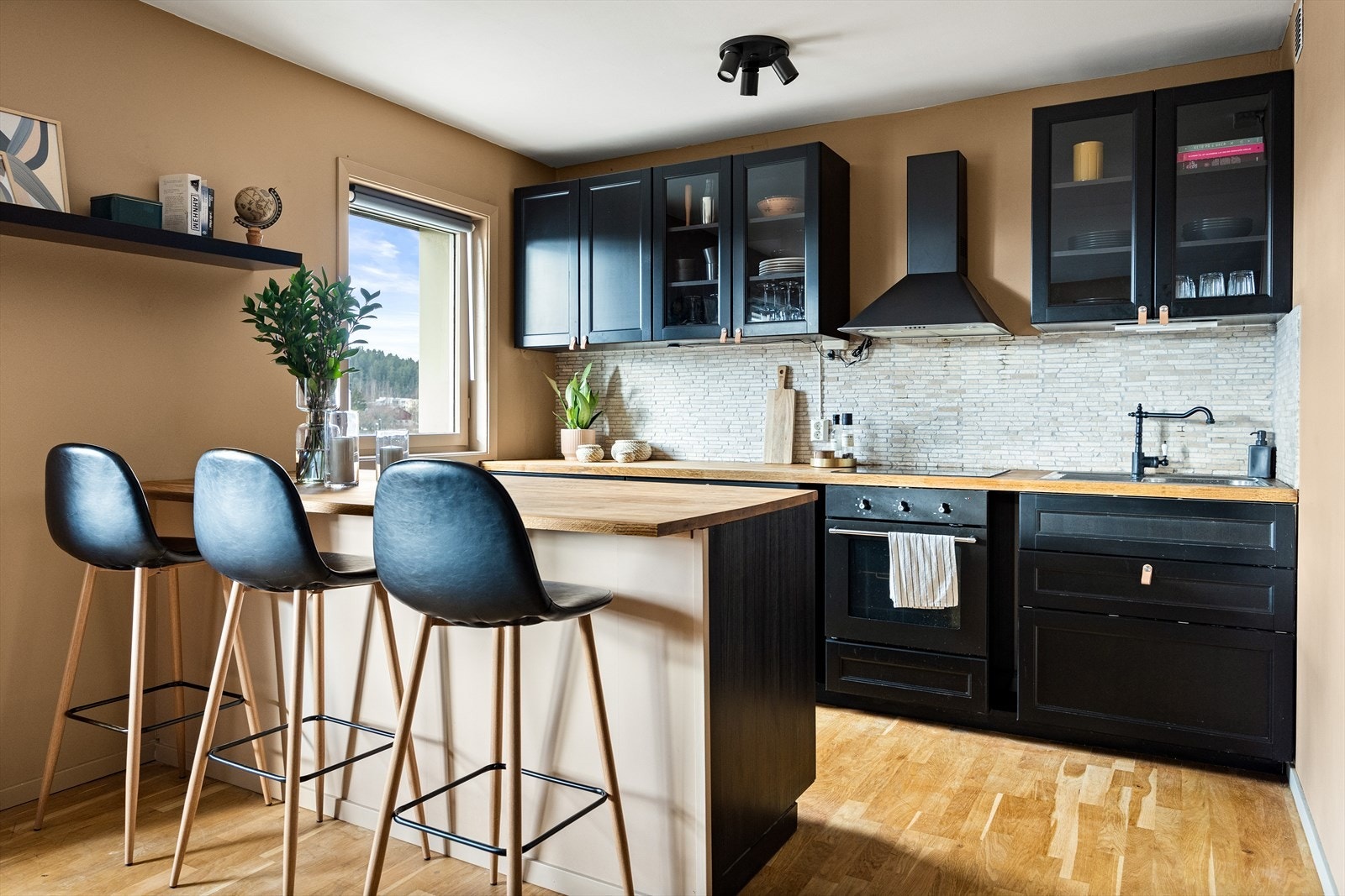 Kjøkkeninnredning med profilerte fronter, heltre benkeplate med nedfelt vaskekum, fliser over benkeplaten og overskap m/glass. Galleribilde