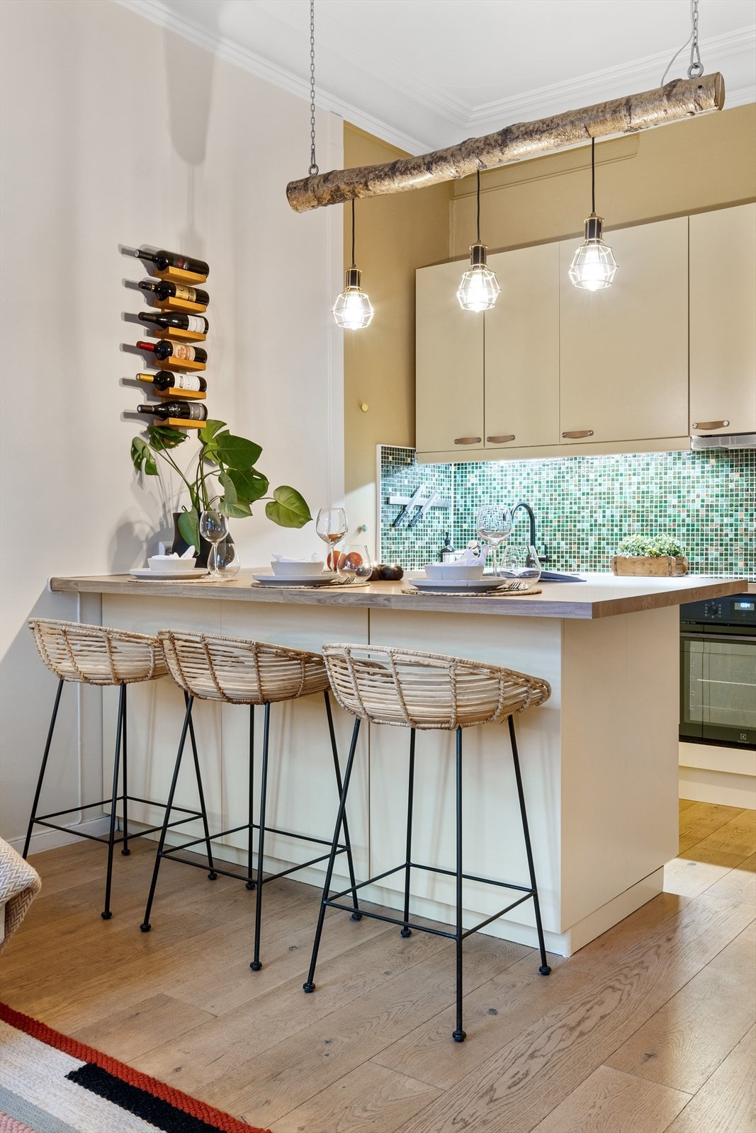 Kjøkkeninnredning med glatte fronter, laminat benkeplate med nedfelt vaskekum, samt fliser og belysning over benkeplaten. Kjøkkenøy med barstoler. Galleribilde