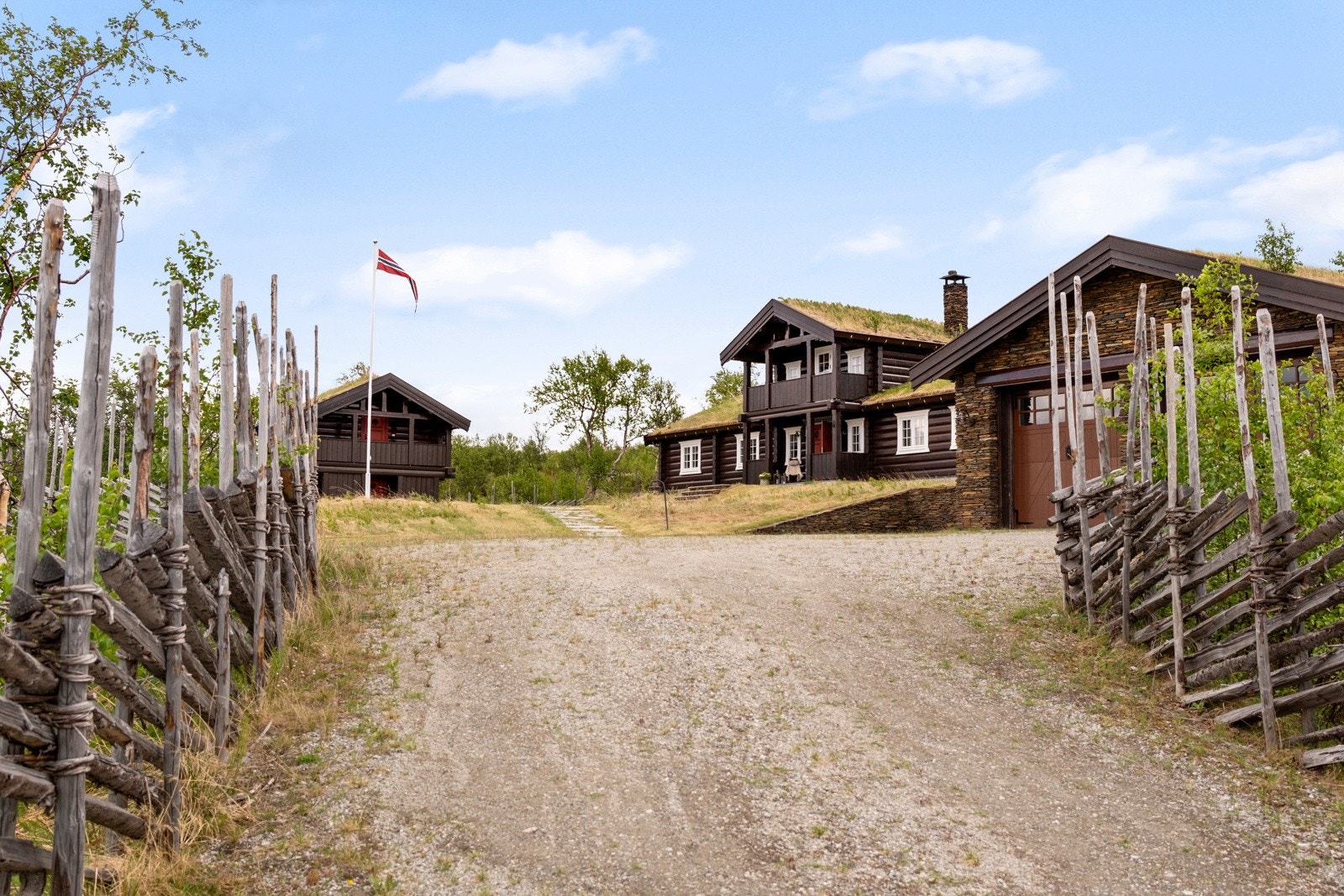 Gårdsplassen er pent opparbeidet med grus og steinheller, omkranset av gjerde og frodige grøntarealer. Galleribilde