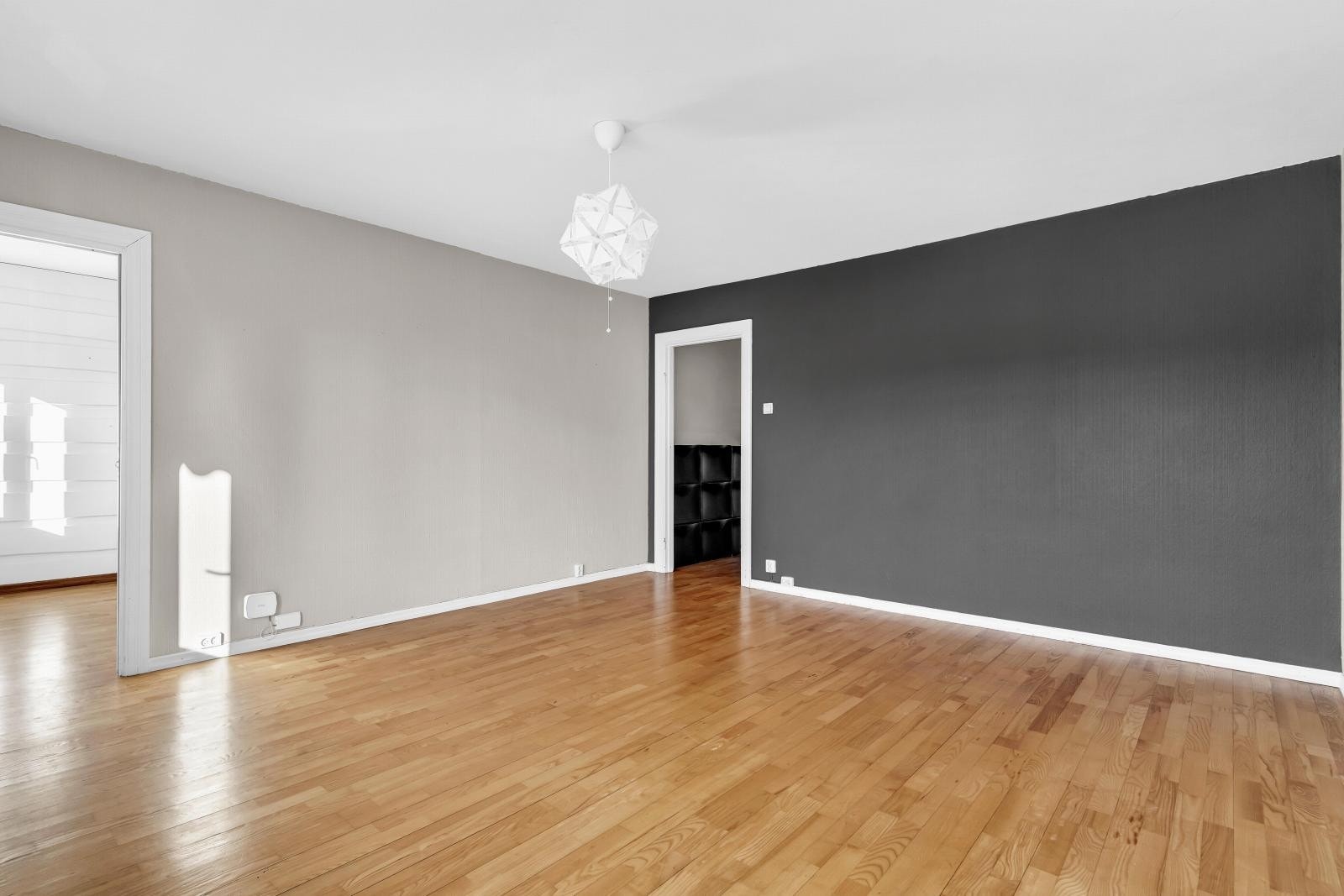 Stuen har lyse vegger, en mørk kontrastvegg og parkettgulv. Rommet er romslig med moderne taklampe og naturlig lys fra vinduene. Galleribilde