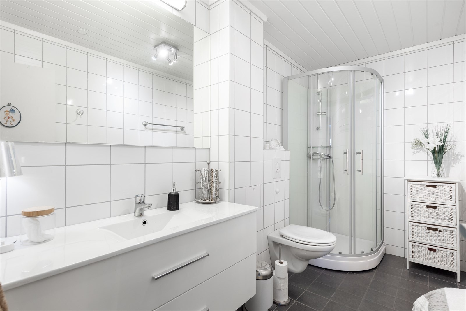 Badet fra 2016 er helfliset med varmekabler i gulv og har hvit innredning med dype skuffer og heldekkende servant. Speil på vegg med overlys. Badet er også innredet med dusjkabinett og veggmontert toalett. Galleribilde