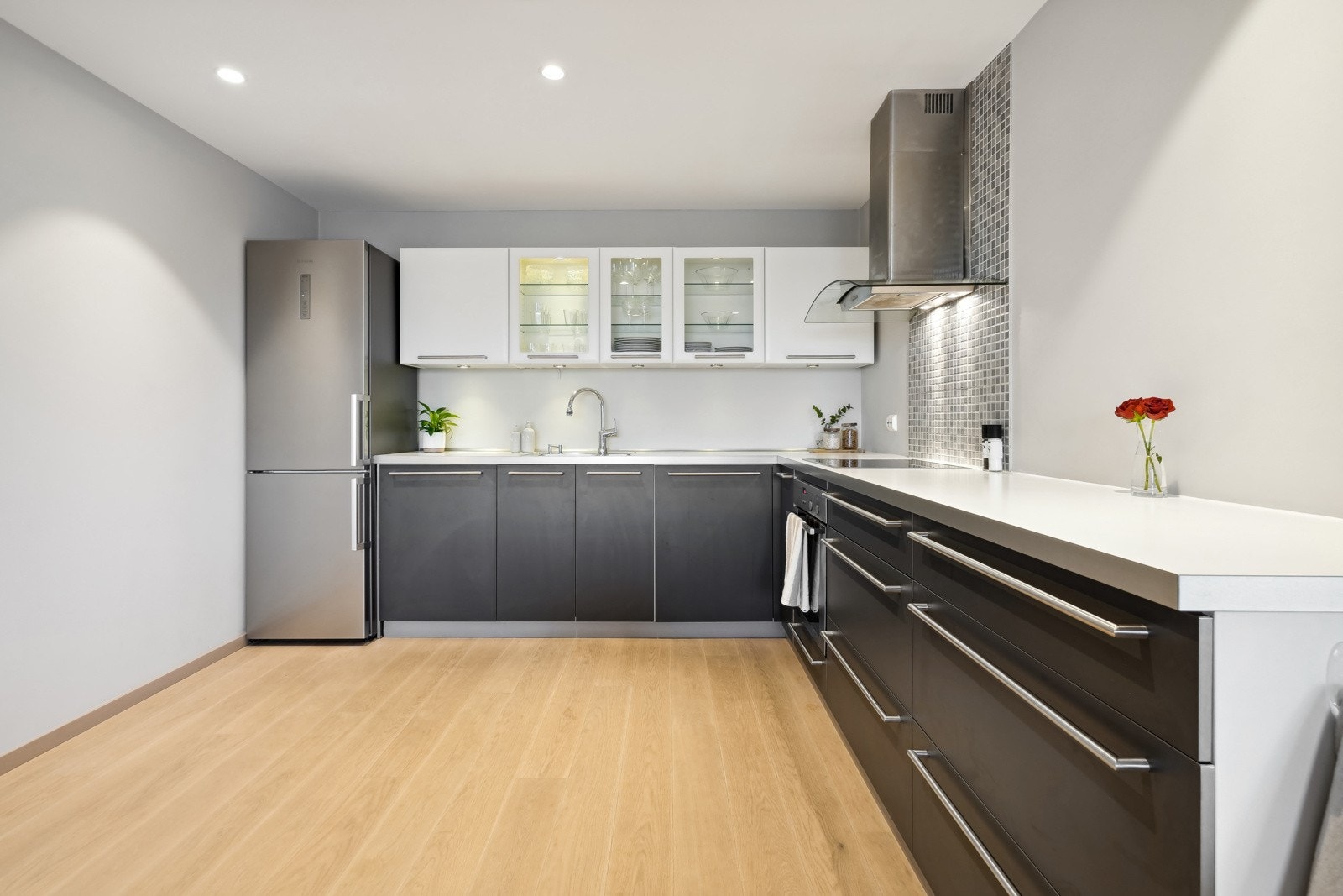 Kjøkkenet har mørke underskap og skuffer, og lyse overskap med tre vitrineskap. Laminat benkeplate Galleribilde