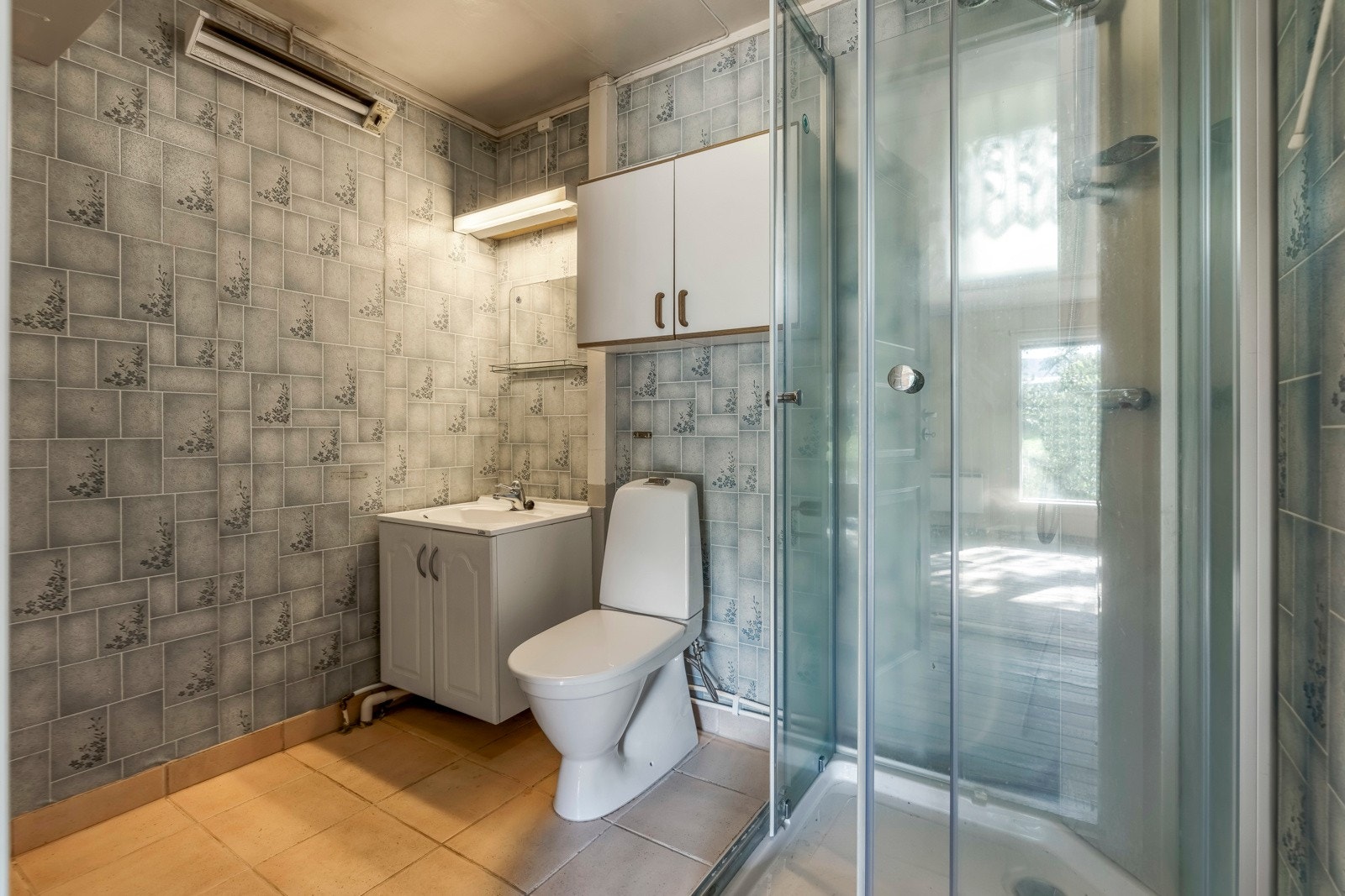 Badet er bestående av servant med underskap, gulvstående toalett og dusjkabinett Galleribilde