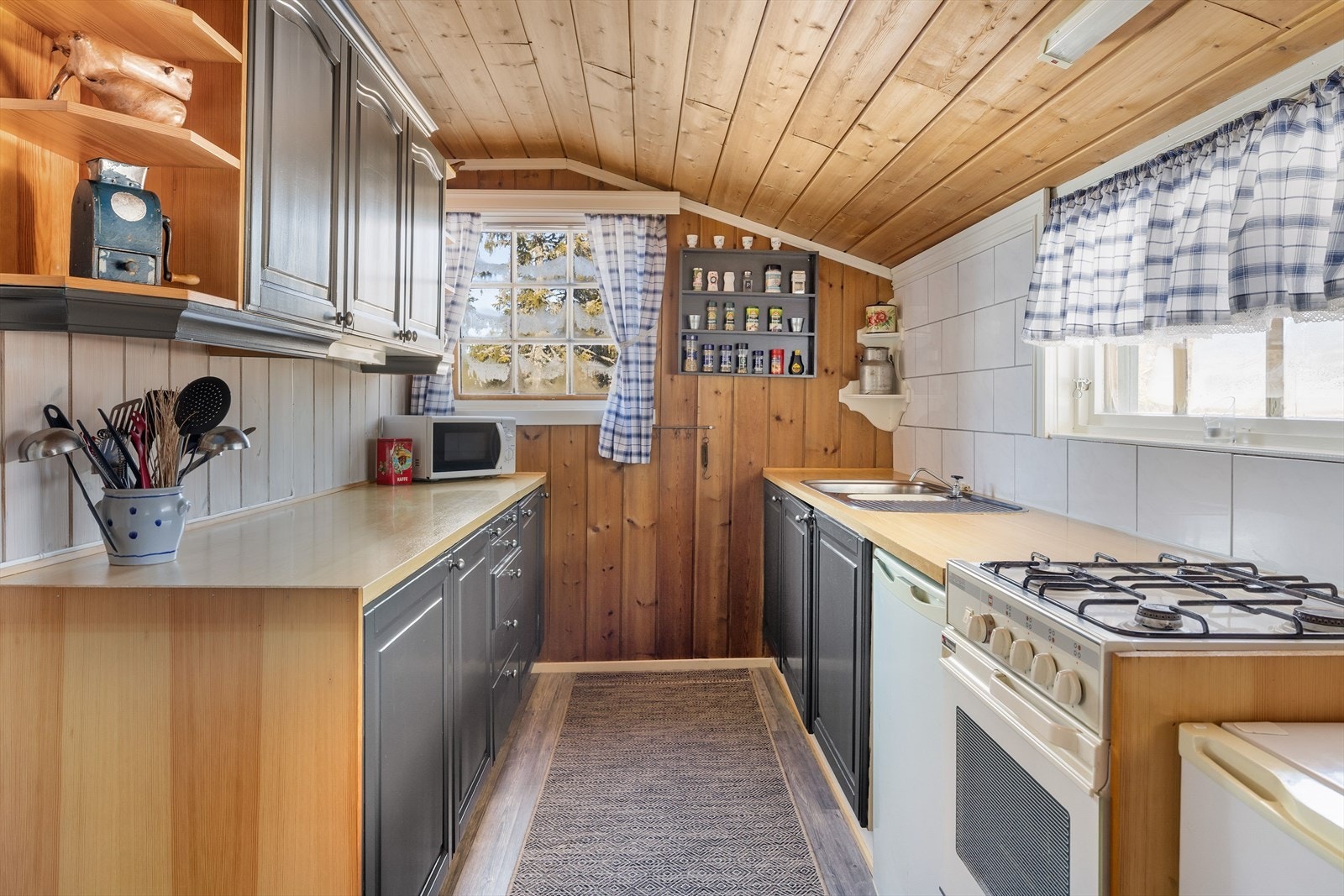 Furukjøkken med malte profilerte fronter, laminert benkeplate med nedfelt kum og fliser i benkeryggen. Vann fra vannbeholder med elektrisk pumpe og avløp med rør ut til terreng. Galleribilde