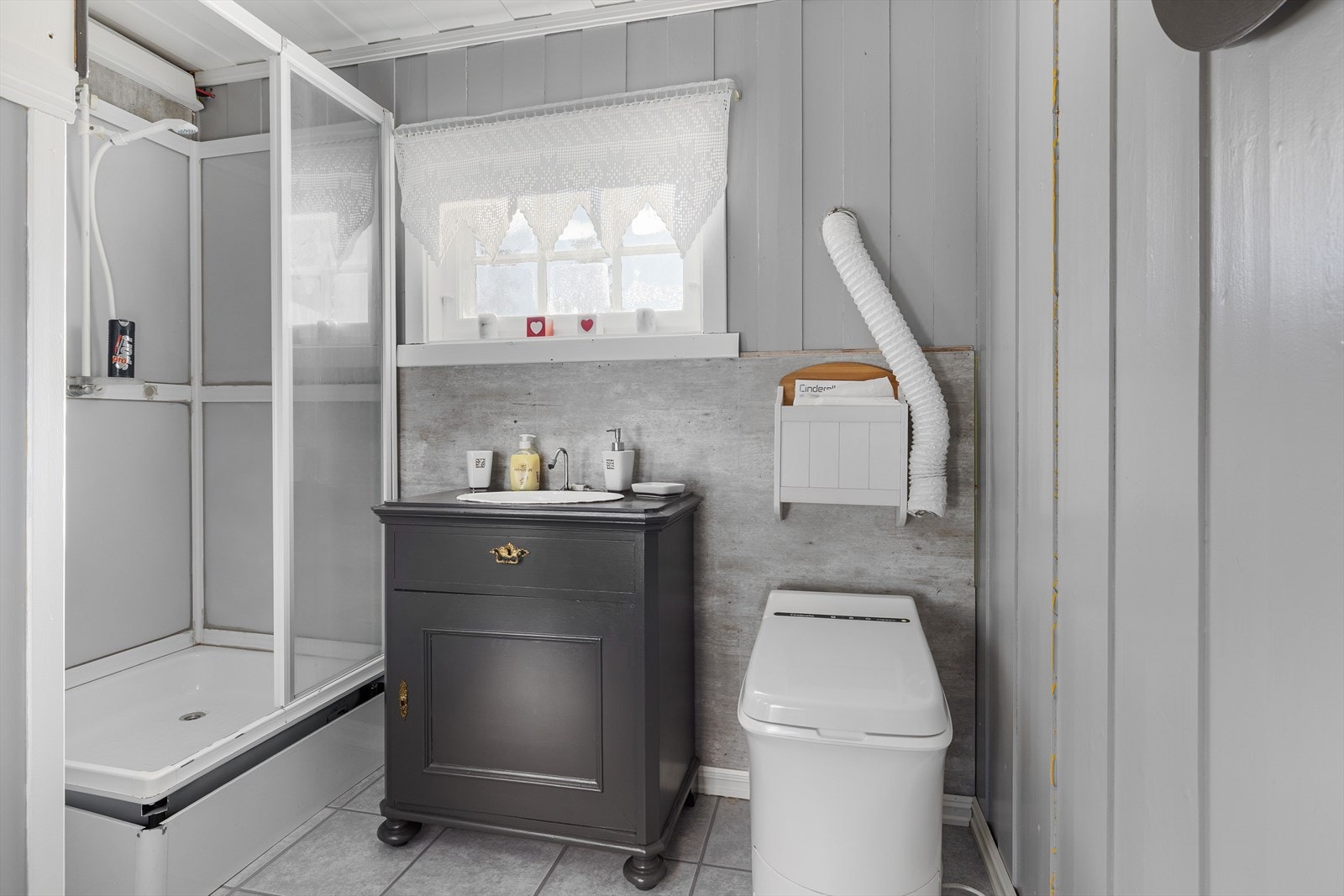 Lyst enkelt baderom uten sluk/avløp. Rommet har laminat på gulv, malt trepanel på veggene og et vindu som slipper inn naturlig lys. I 2022 ble det satt inn toalett Cinderella forbrenningsovn på baderom. Galleribilde