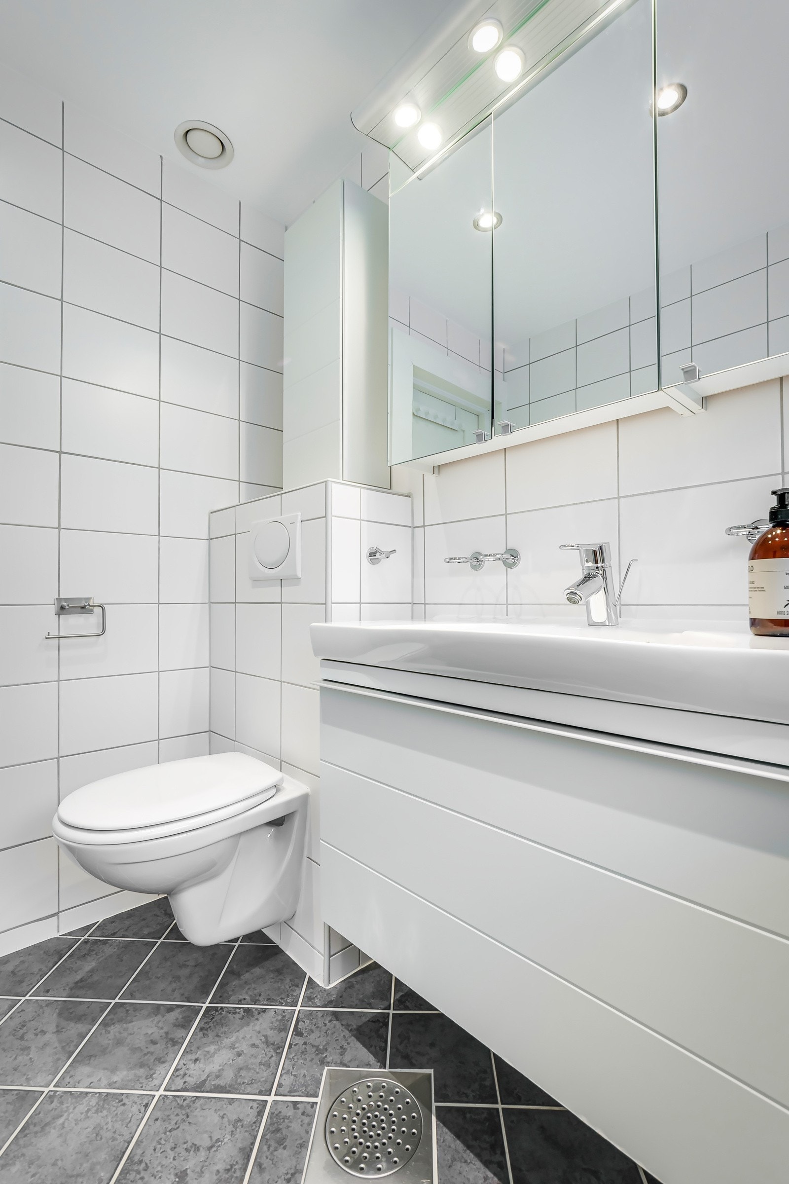 Moderne baderomsinnredning med skuffer og heldekkende servant, speilskap med belysning over. Galleribilde