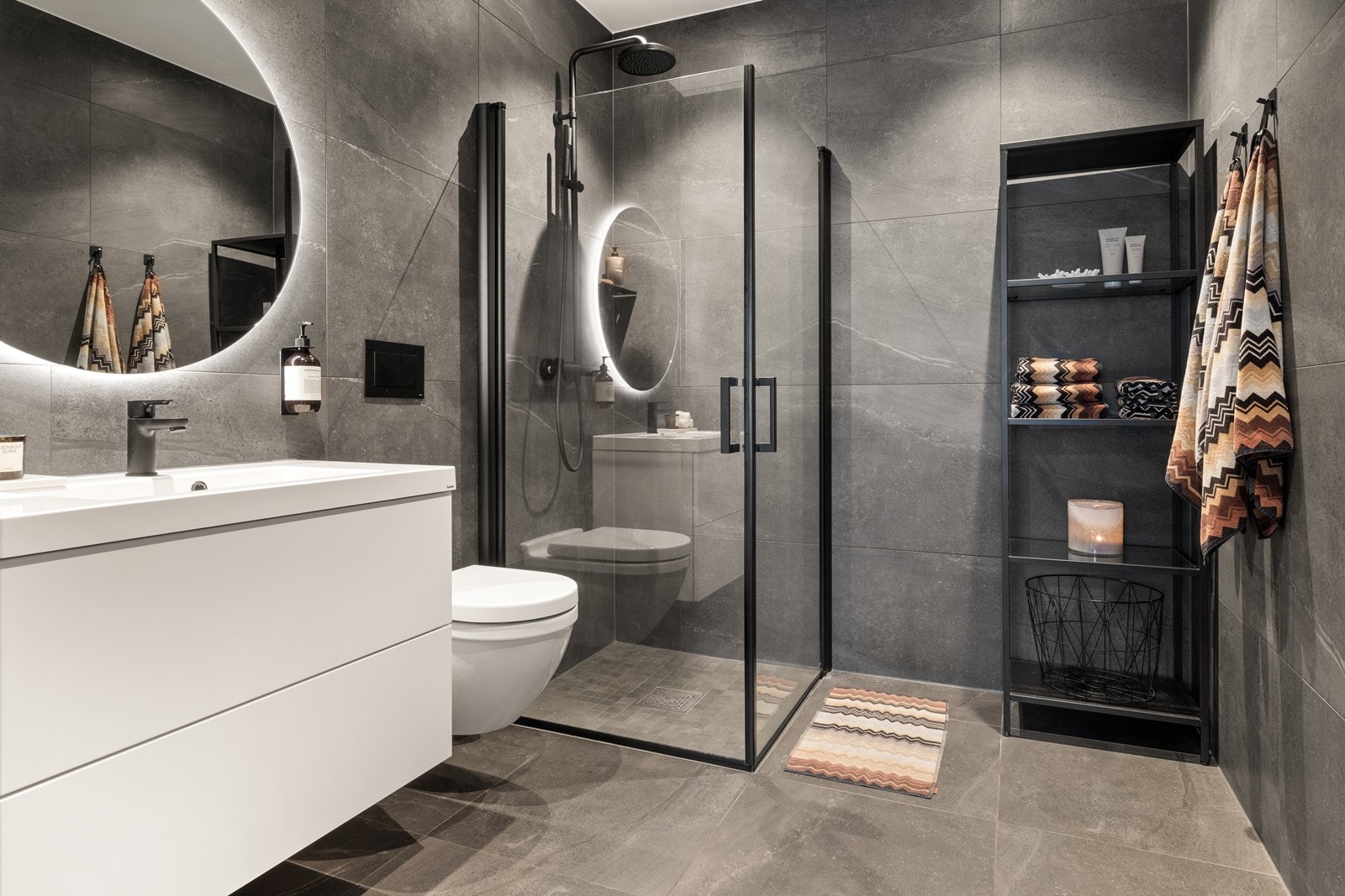 De koksgrå, store flisene og sorte detaljer på armaturer, trykkplate og dusjvegger og speil med integrert belysning er det virkelig et lekkert og delikat bad. Galleribilde