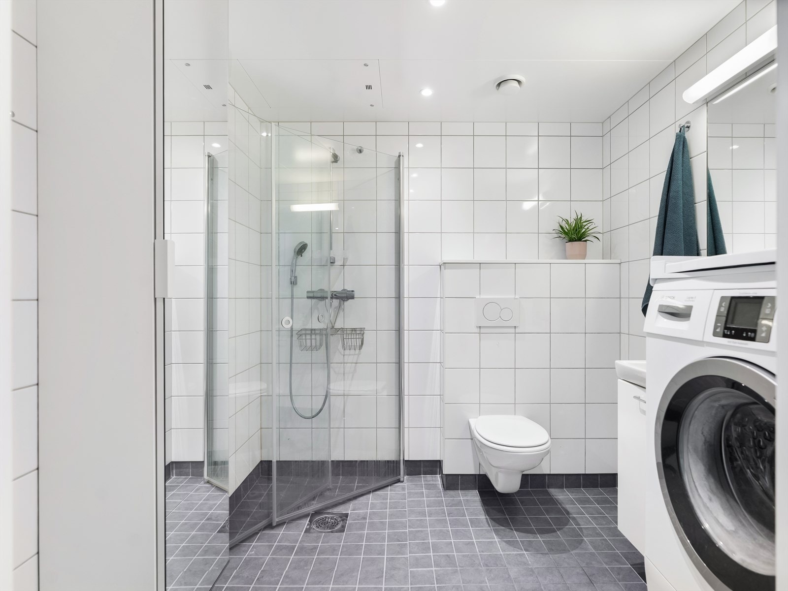 Lyst og moderne bad med fliser på både gulv og vegger. Innredningen består av underskap med servant, speil, og armatur med stikkontakt. Dusjsonen har dusjing direkte på gulv og vegg. Galleribilde
