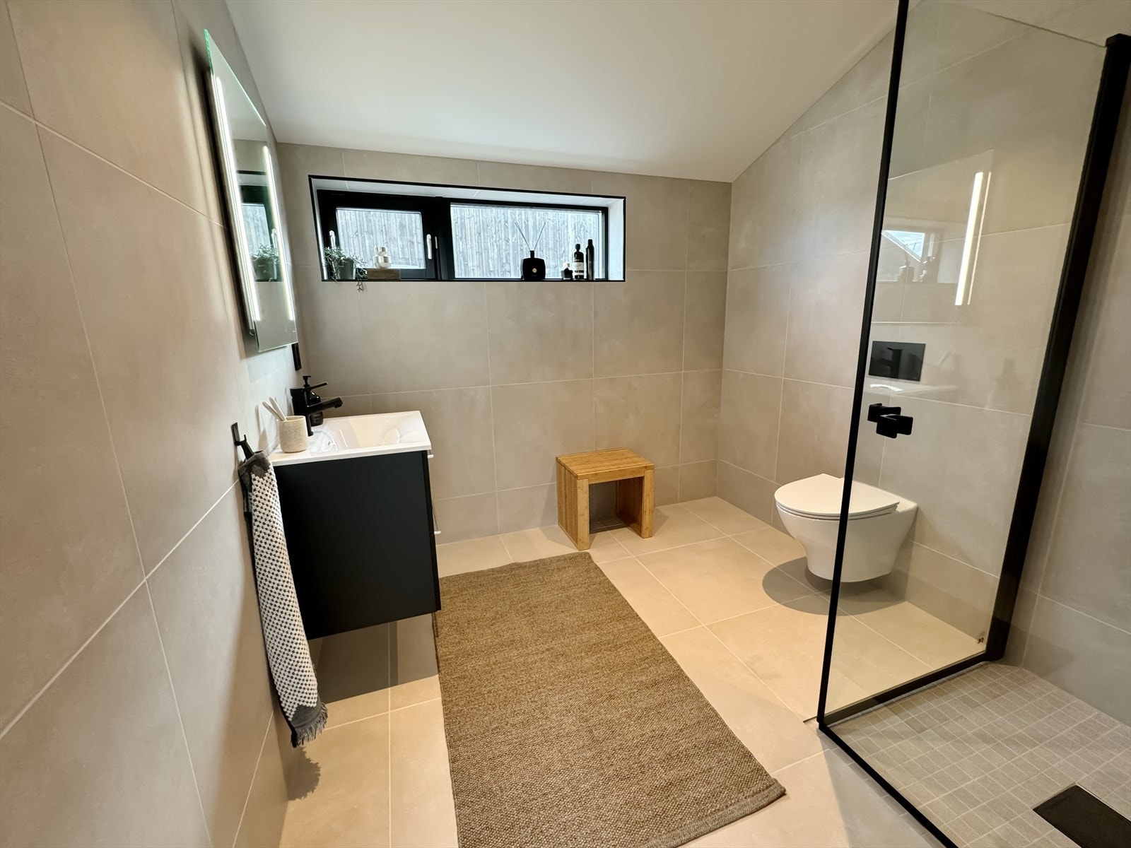 Moderne, delikat baderom med god takhøyde. Fliser i dus fargetone og lekre sorte detaljer. Galleribilde