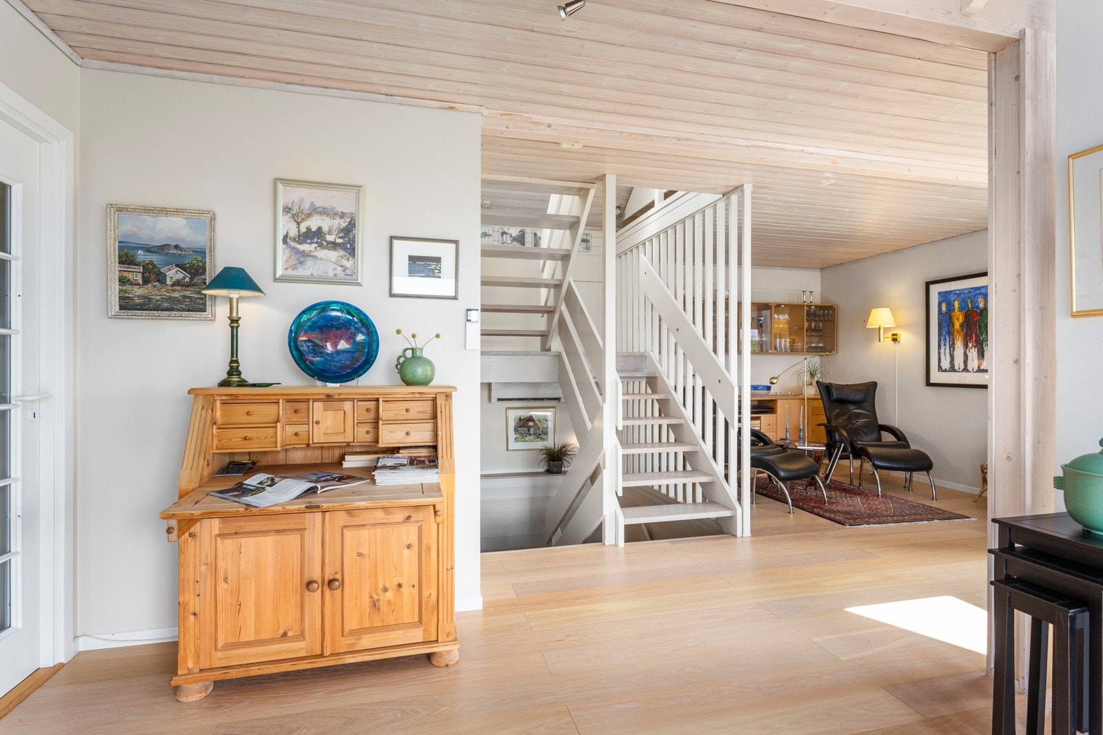 Stuen har himmelsk takhøyde, enstavs eikeparkett på gulvet mot lyse veggflater og skrå himling, noe som gir et stilrent uttrykk. Galleribilde