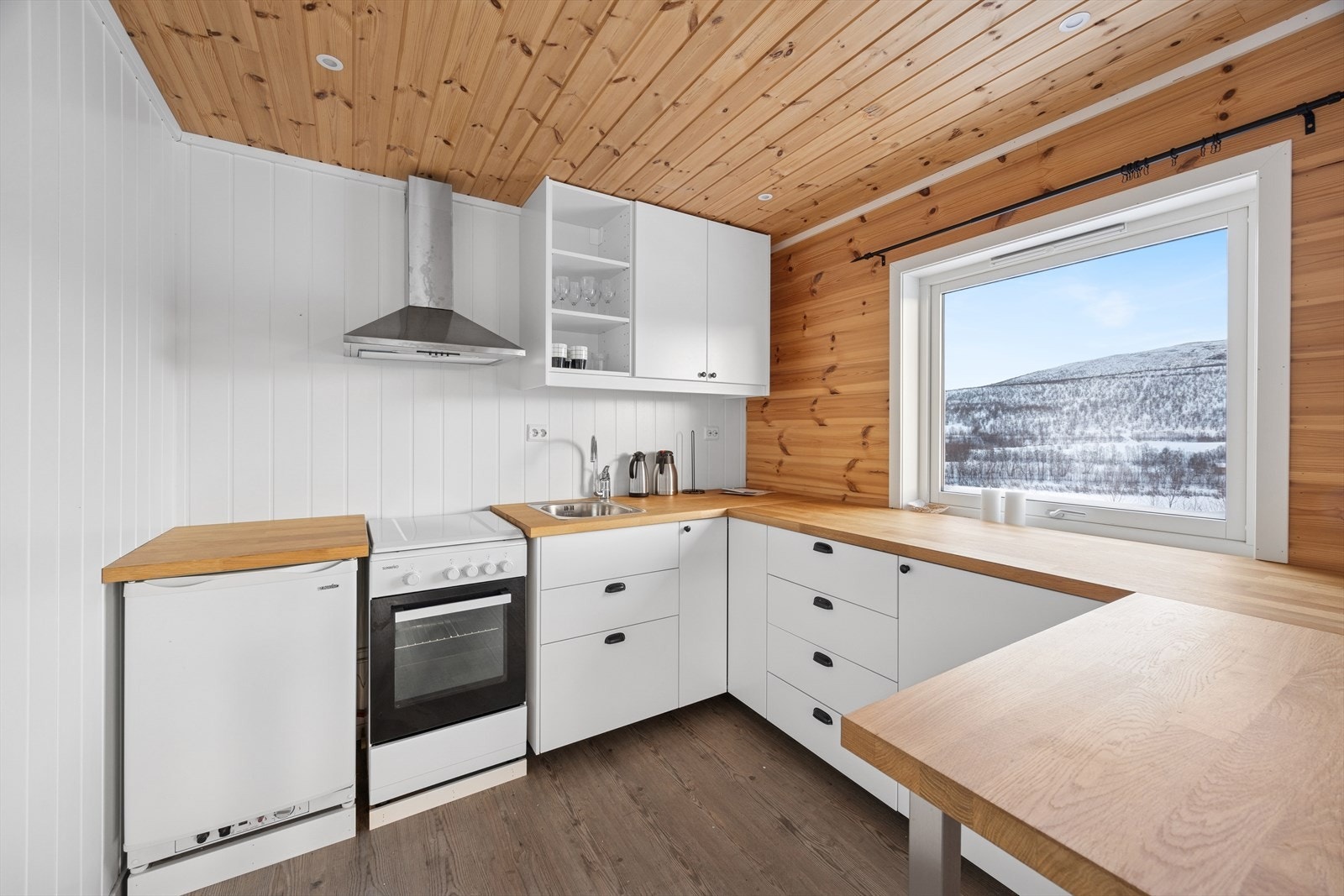 Kjøkkenet er utstyrt med moderne innredning med glatte fronter og en heltre benkeplate med nedfelt vaskekum, som gir et stilrent og funksjonelt preg. Galleribilde