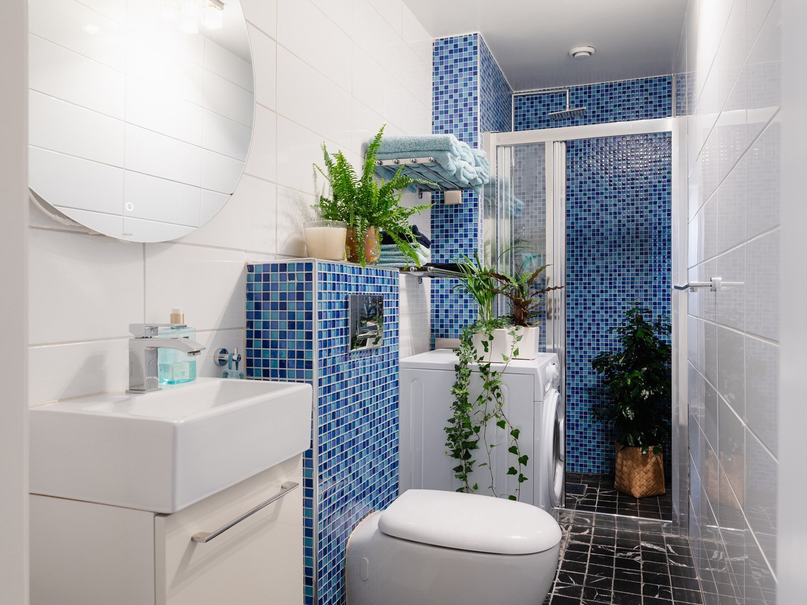 Badet er flislagt, med lyse avlange gliser og mosaikkfliser i kontrast. Galleribilde