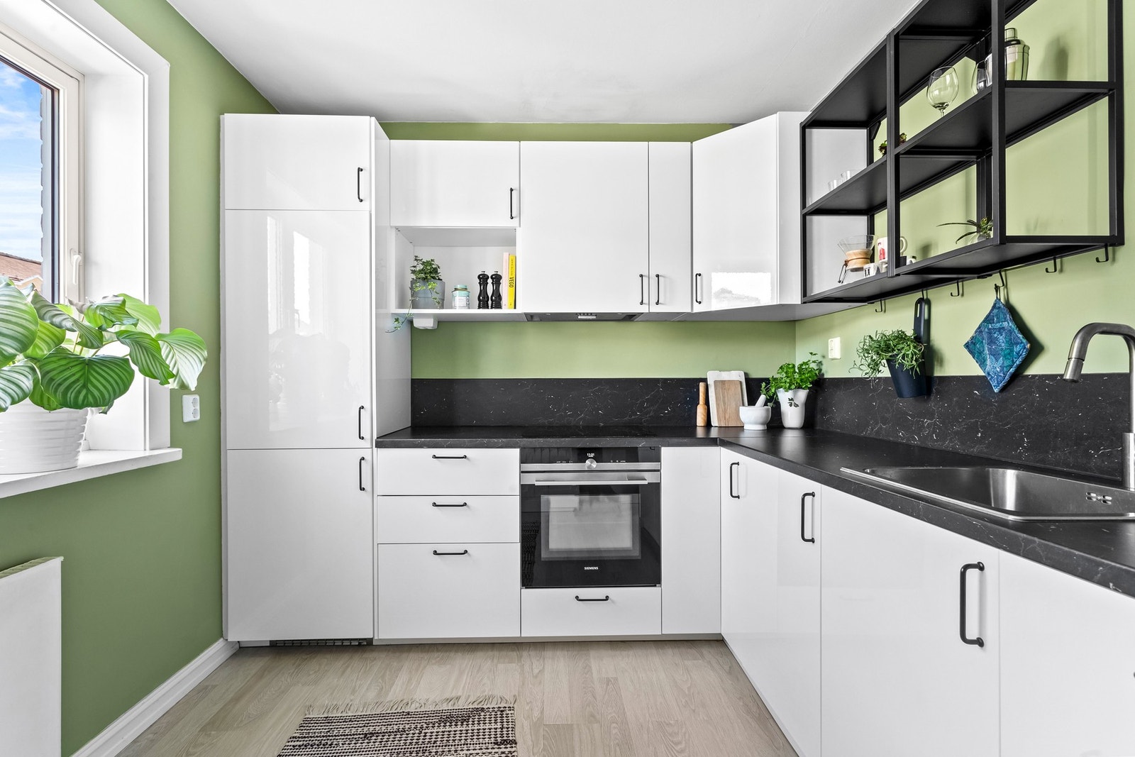 Hvite, glatte høyglans fronter gir et rent og ryddig uttrykk, mens åpne hyller over benken tilbyr lett tilgjengelig oppbevaring for dine oftest brukte ting. Galleribilde