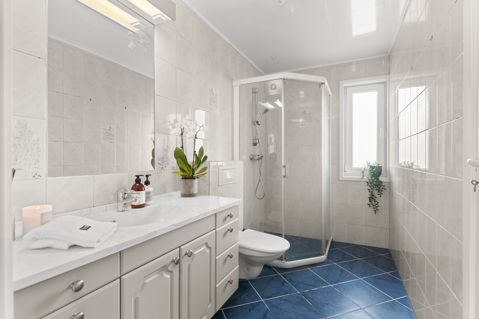 Bad med fliser på vegger og gulv. Dusjnisje, servant med underskap og toalett. Galleribilde