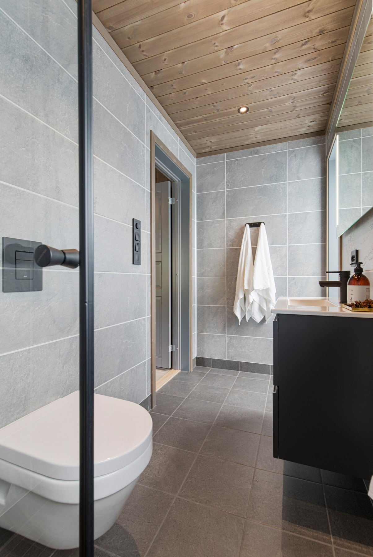 Utstyrt med vegghengt toalett, dusjhjørne med glassdører og innredning med skuffefronter med grepskant. Speil med belysning over servant. Galleribilde