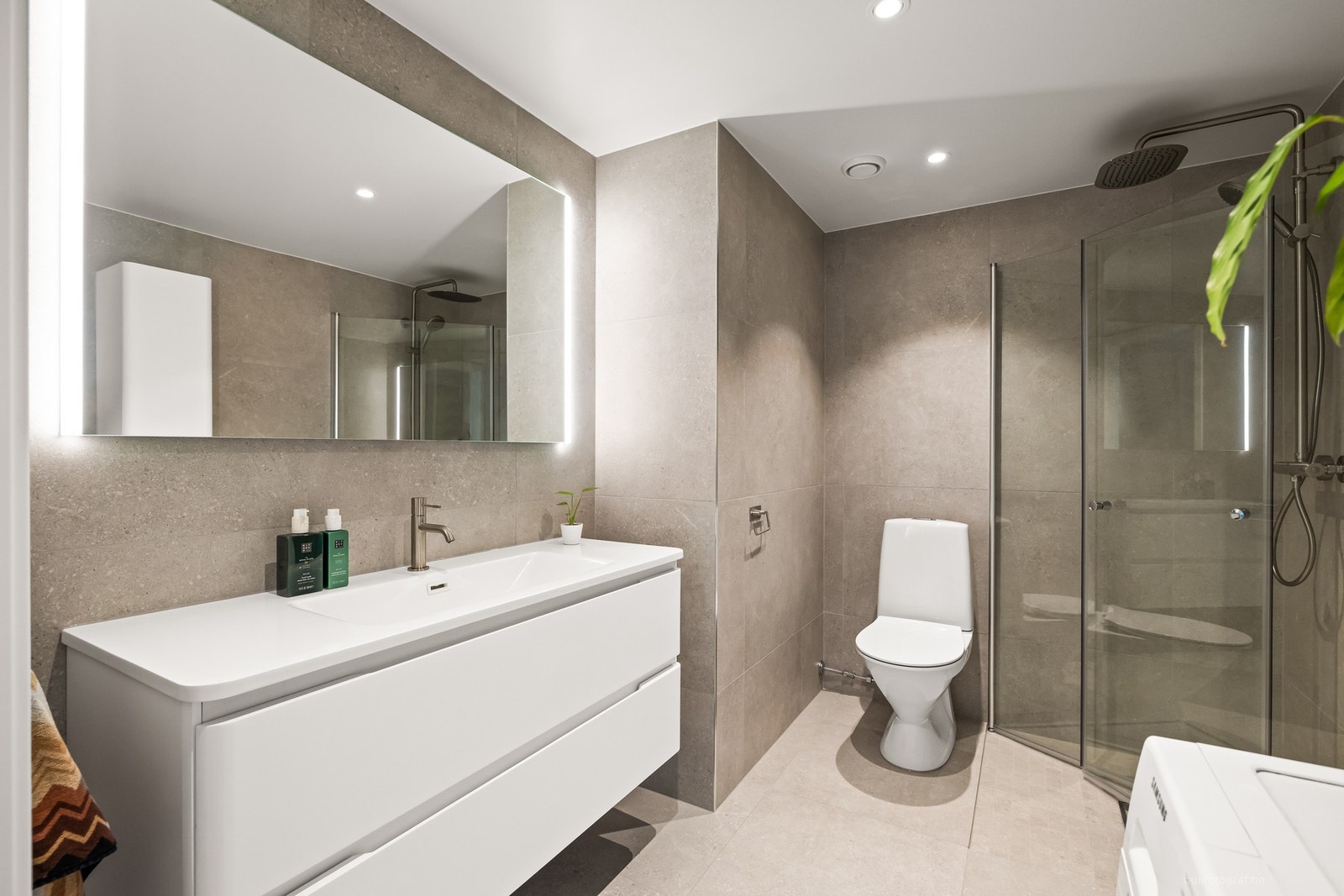 Badet har en romslig servant med underskap, dusjhjørne, klosett og opplegg for vaskemaskin Galleribilde