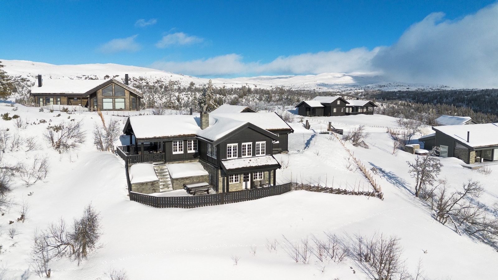 Utvendig fasade er kledd med panel og deler av hytta er forblendet med tørrmurte overflater Galleribilde