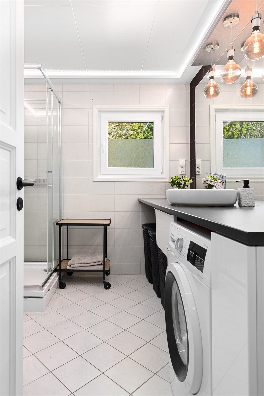 Badet er innredet med dusjkabinett, vegghengt toalett og et romslig baderomsmøbel med skuffer, skap og benkeplate. Opplegg for vaskemaskin. Galleribilde