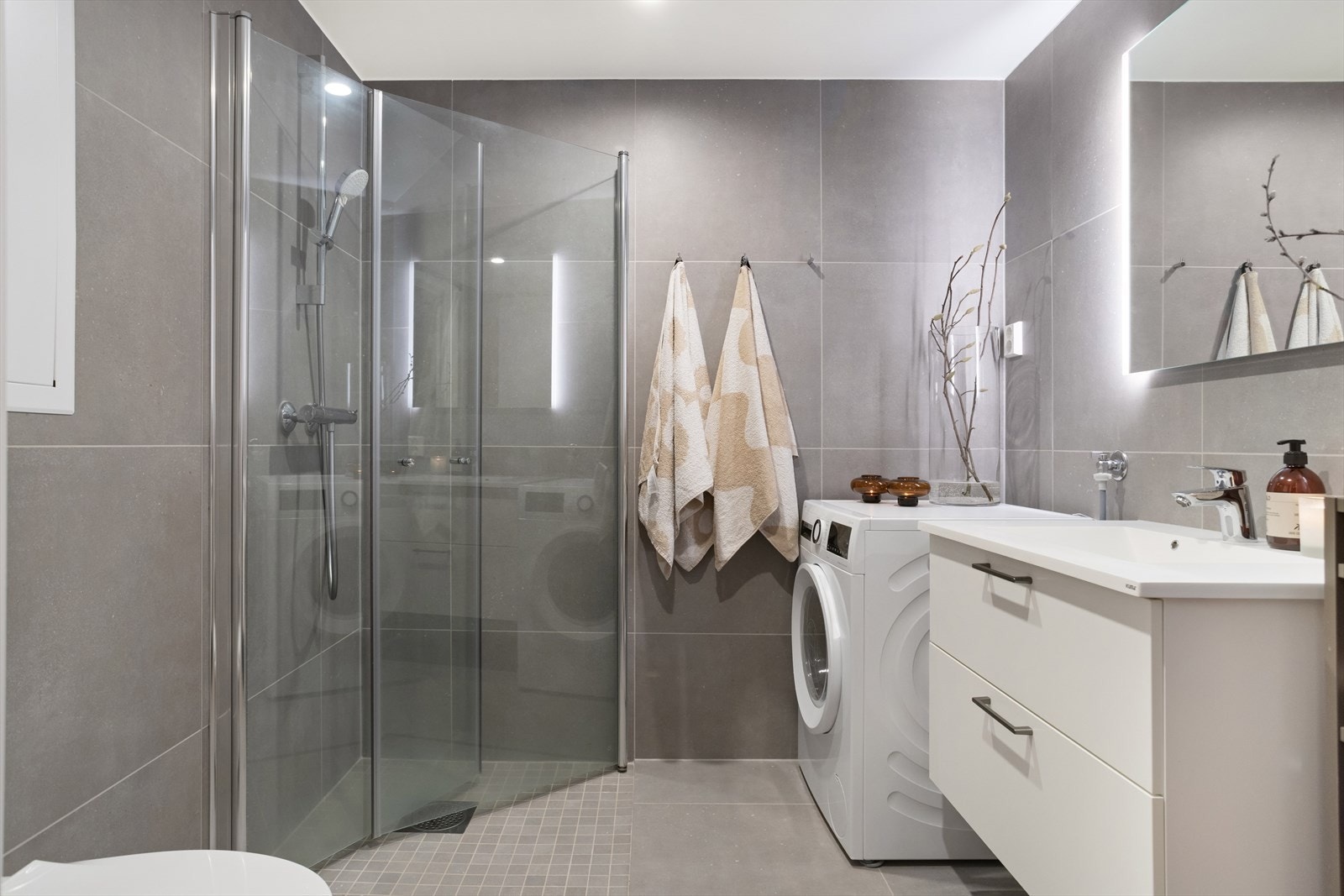 Baderommet er ca 4,2 m² og har flis på gulv og vegg, malt slett himling. Dusjvegger av glass, vegghengt toalett, innredning med servant samt opplegg for vaskemaskin. Galleribilde