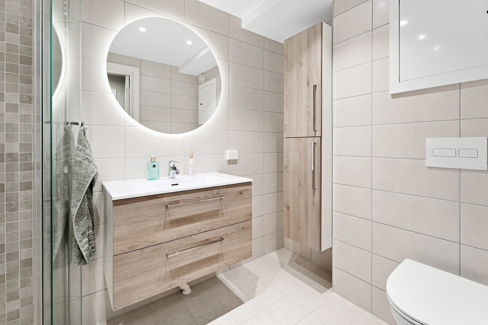 Badet er utstyrt med vegghengt servantinnredning med skuffer og ett-greps armatur, vegghengt speil med lys og vegghengt toalett med innebygget sisterne, samt dushjørne med leddet glassdører og dusjarmatur tilkoblet veggmontert hånddusj og regndusj. Galleribilde