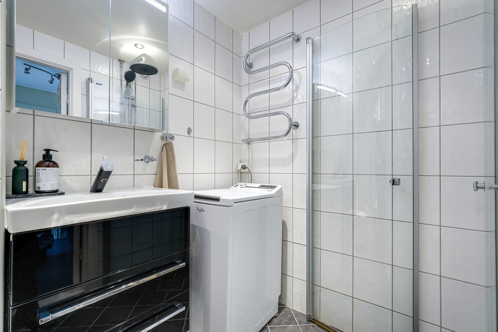 Moderne innredning med høyglans baderomsinnredning, speilskap med integrert belysning, servant og håndkletørker på vegg. Galleribilde