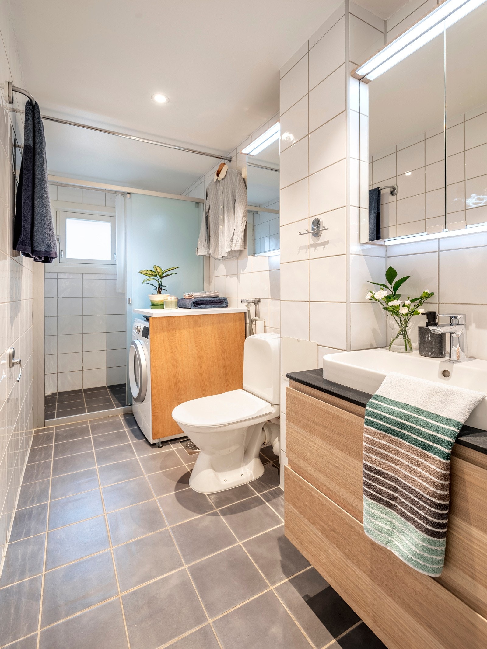 Badet er praktisk plassert i tilknytning til entréen og er pent innredet med fliser på vegger og gulv, varmekabler og malt slett himling med innfelt downlights. Galleribilde