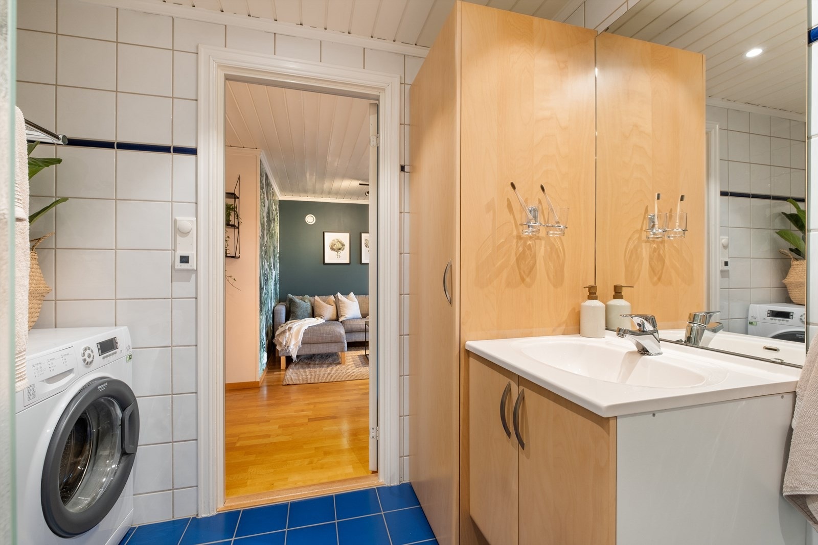 Badet er innredet med servant i innredning med skap, speil med belysning på vegg, dusj med innfellbare glassdører og vegghengt toalett samt opplegg for vaskemaskin Galleribilde