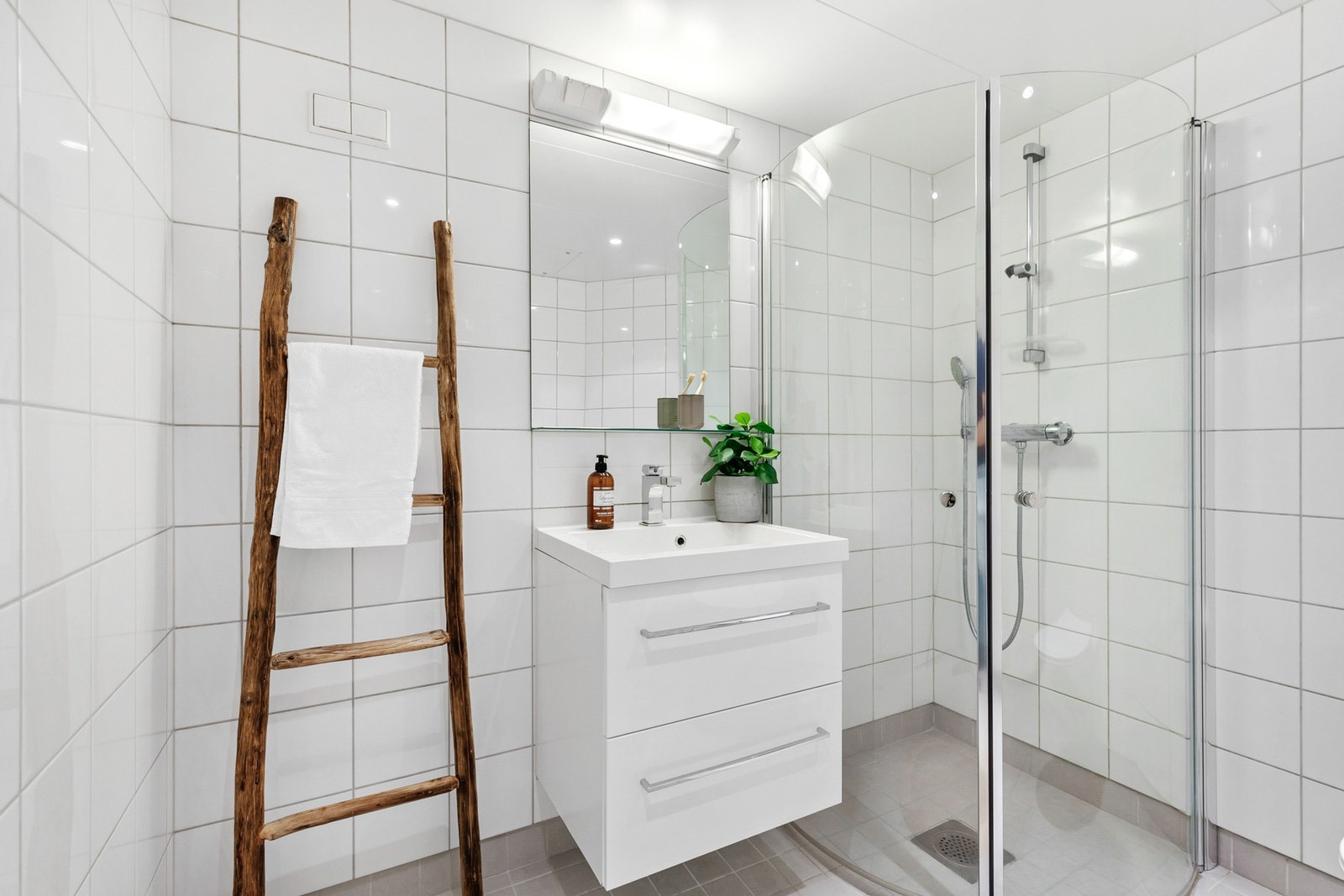 Badet er innredet med dusjhjørne med innfellbare glassdører, vegghengt toalett og opplegg for vaskemaskin Galleribilde
