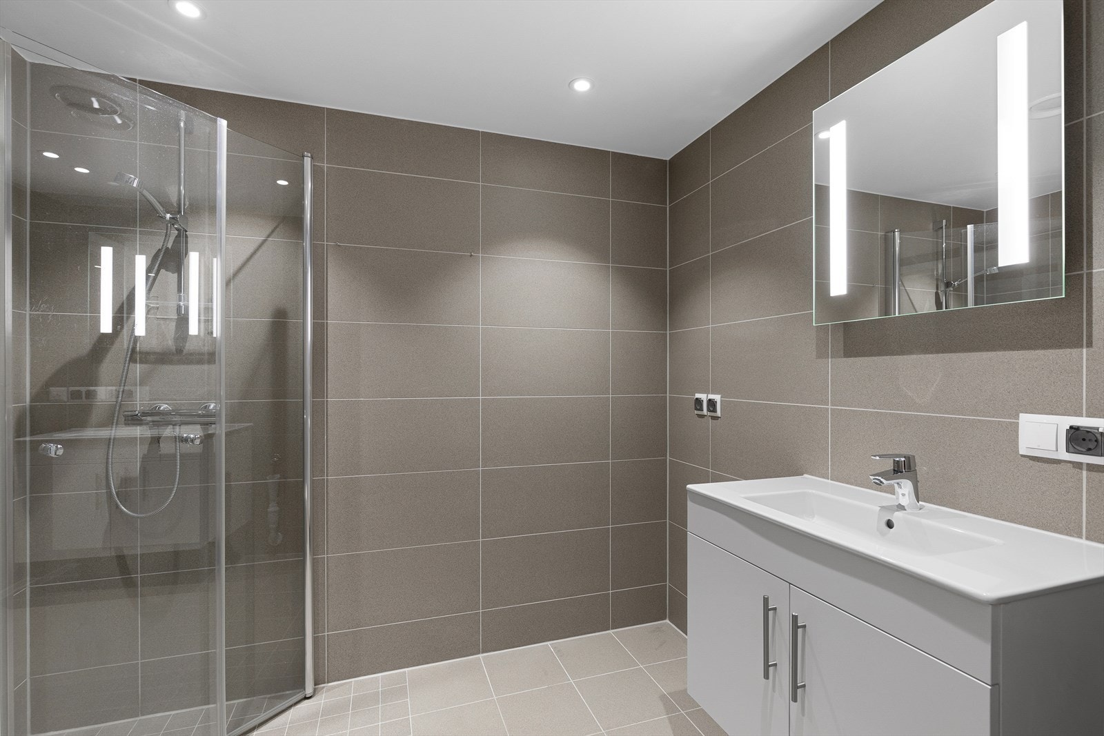 Delikat stort baderom med dusjnisje og moderne baderomsinnredning. Det er opplegg for vaskemaskin. Galleribilde