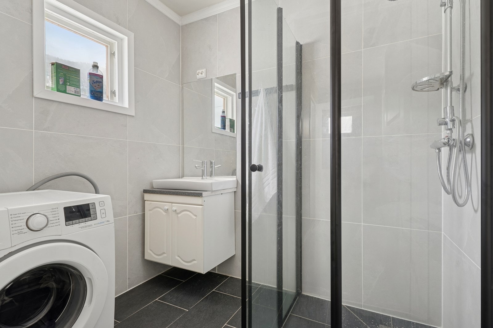 Baderommet er nyoppusset i 2024 og har mørke fliser med varme i gulv, og lyse overflater på vegger og i himling. På badet er det også plass til vaskemaskin. Galleribilde