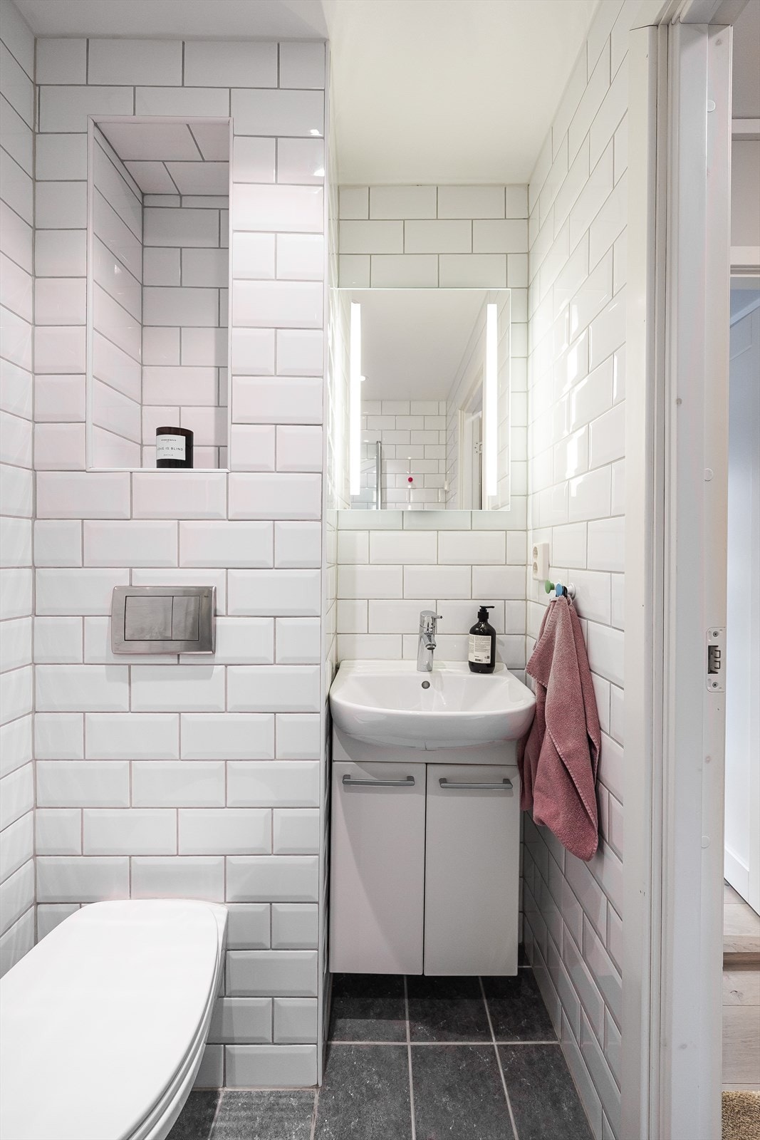 Nedsenket himling med malt flate og downlights, samt vegghengt servantskap med glatte fronter. Speil med integrert lys og vegghengt toalett. Galleribilde