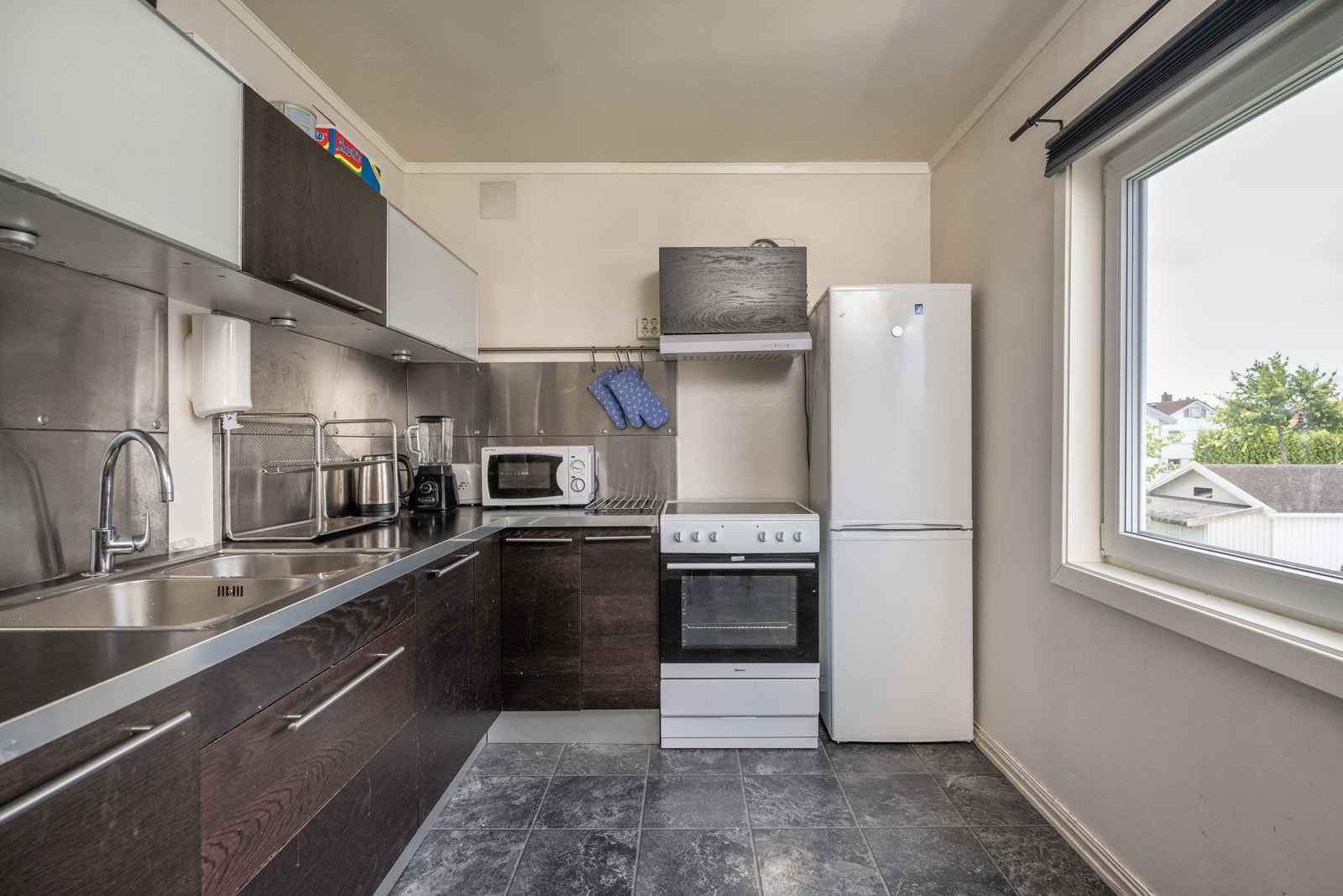 Sort kjøkkeninnredning med glatte fronter og laminat benkeplate. Frittstående kjøleskap med fryser og stekeovn med platetopp. Galleribilde