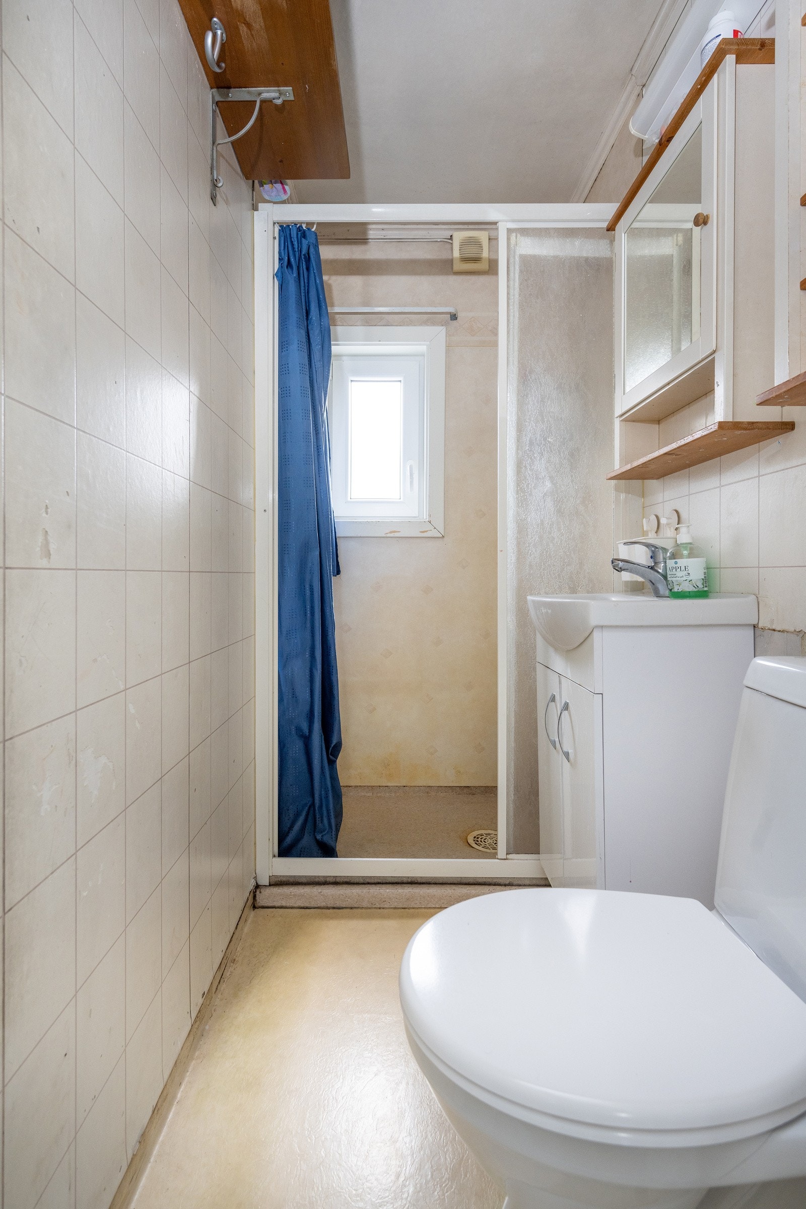 Badet har hvit vegghengt servant med glatte fronter, speil, dusjhjørne og toalett Galleribilde