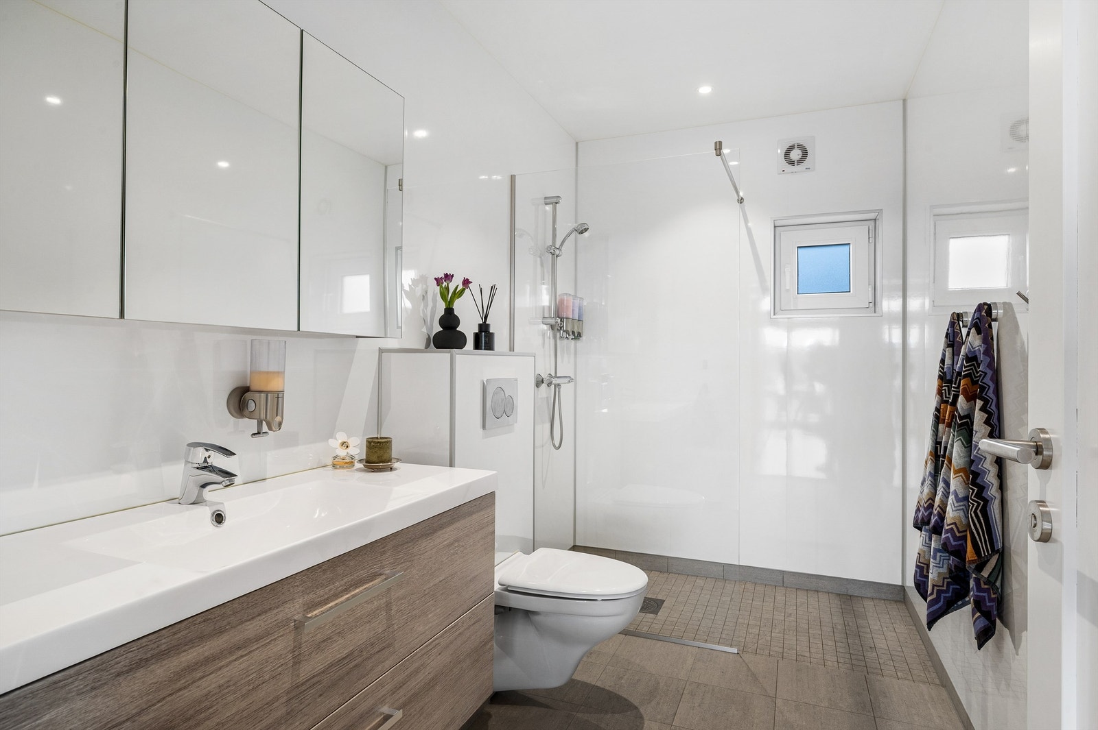 Badet er stilrent og enkelt med stor dusjnisje, wc med innebygget cisterne og servant med skuffer under og speilskap over. Galleribilde