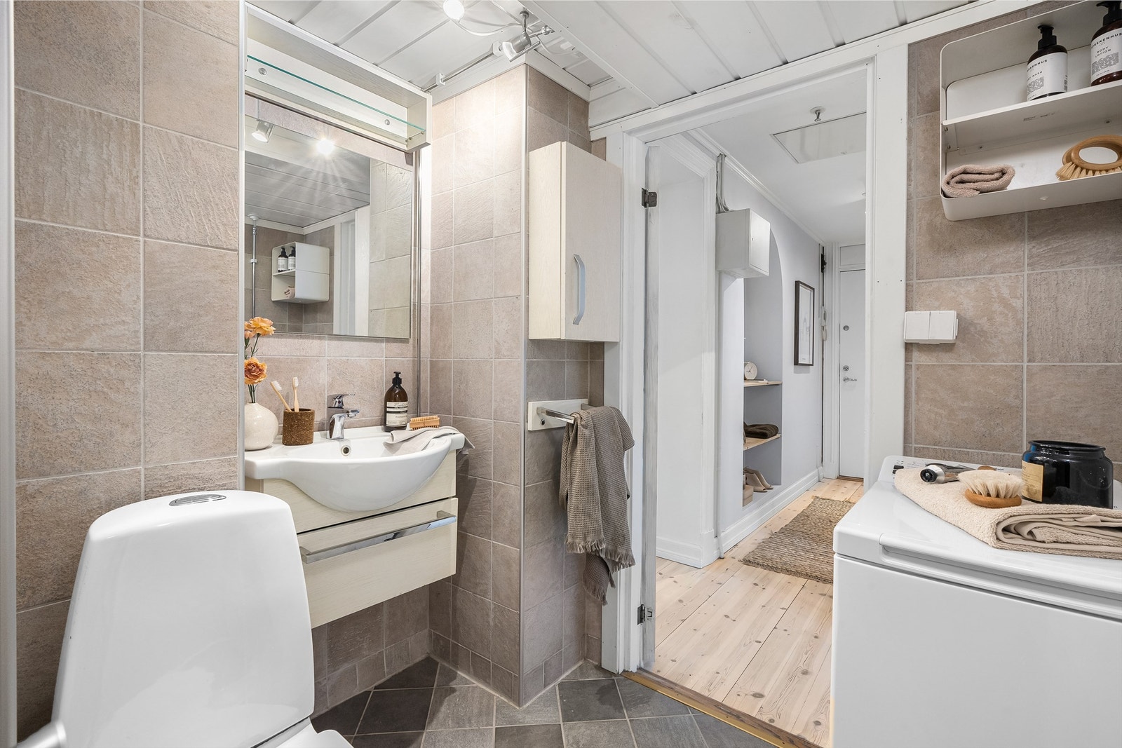 Vegghengt servantskap med ett-greps armatur med speil over. Badet har også et gulvstående toalett og opplegg for vaskemaskin. Galleribilde