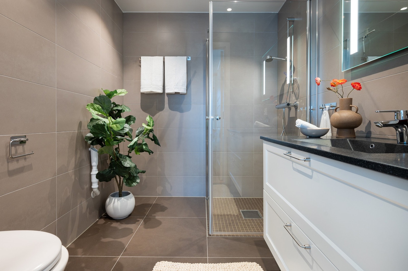 Pent bad med hvit servantinnredning med profilerte fronter, speil, dusj, wc og opplegg til vaskemaskin. Galleribilde