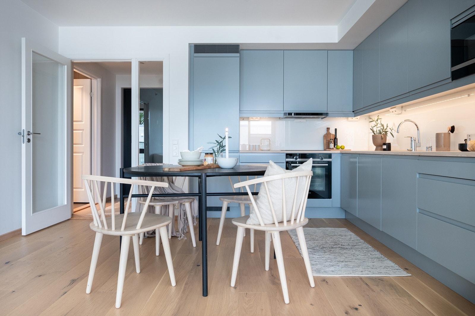 Åpen stue- og kjøkkenløsning med vinkelformet kjøkkeninnredning med lysegrå slette fronter og eikefarget benkeplate i laminat Galleribilde