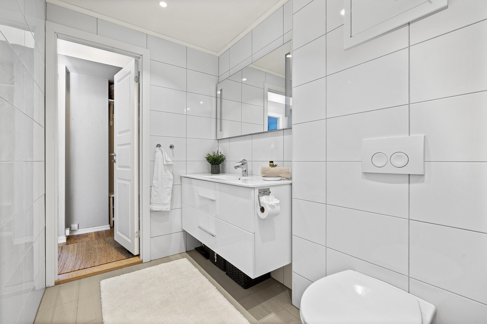 Rommet er utstyrt med servant over skuffeinnredning, speil med belysning, vegghengt toalett og dusjhjørne med innfellbare glassvegger Galleribilde