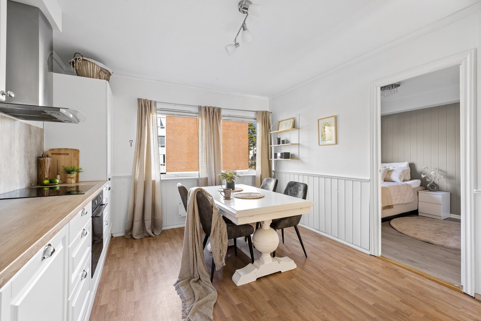 Innredningen har hvite, profilerte fronter og laminert benkeplate med integrerte hvitevarer som kjøleskap/fryseskap, oppvaskmaskin, stekeovn og platetopp Galleribilde