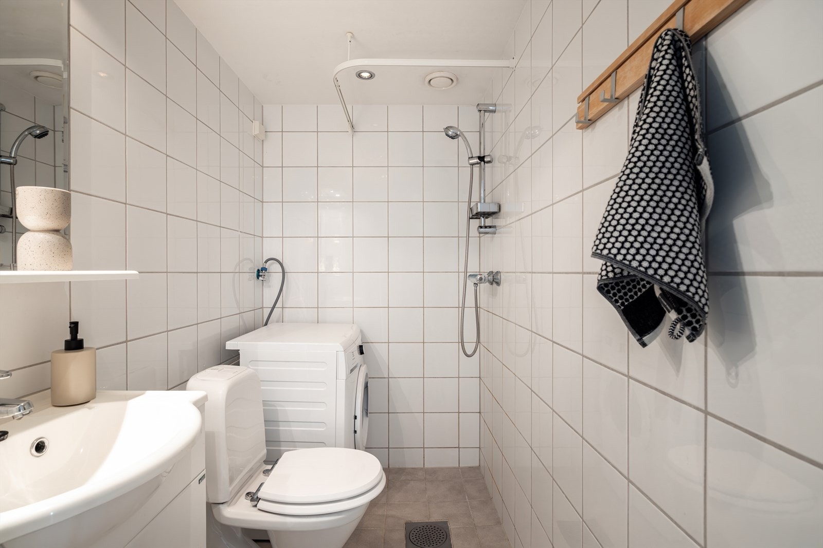 Praktisk flislagt bad fra 2004 med dusjnisje med hånddusj, servant med ett greps blandebatteri og gulvstående toalett. Galleribilde