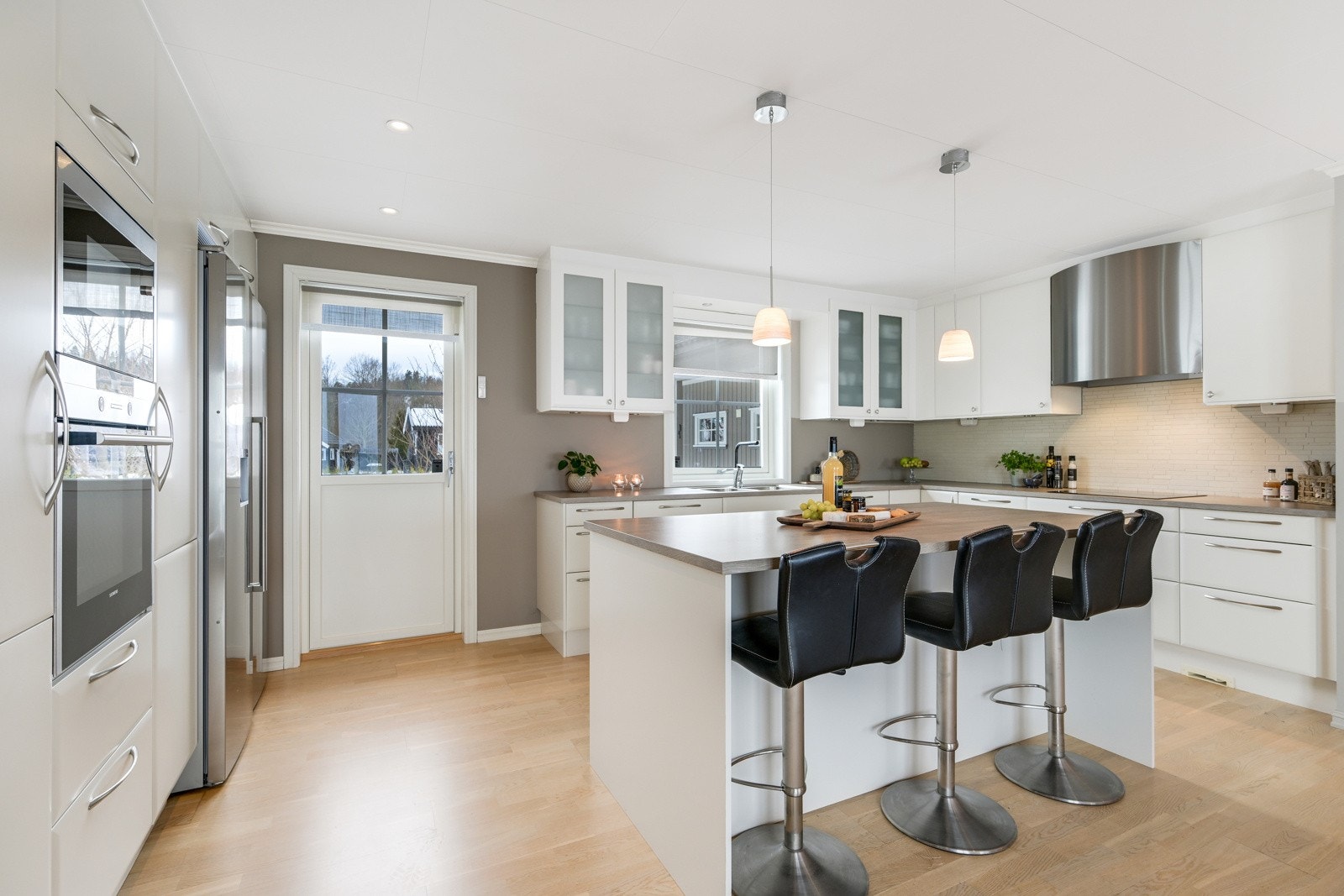 Innredningen har hvite, glatte fronter, store høyskap, frostede vitrineskap og benkeplate av laminat Galleribilde