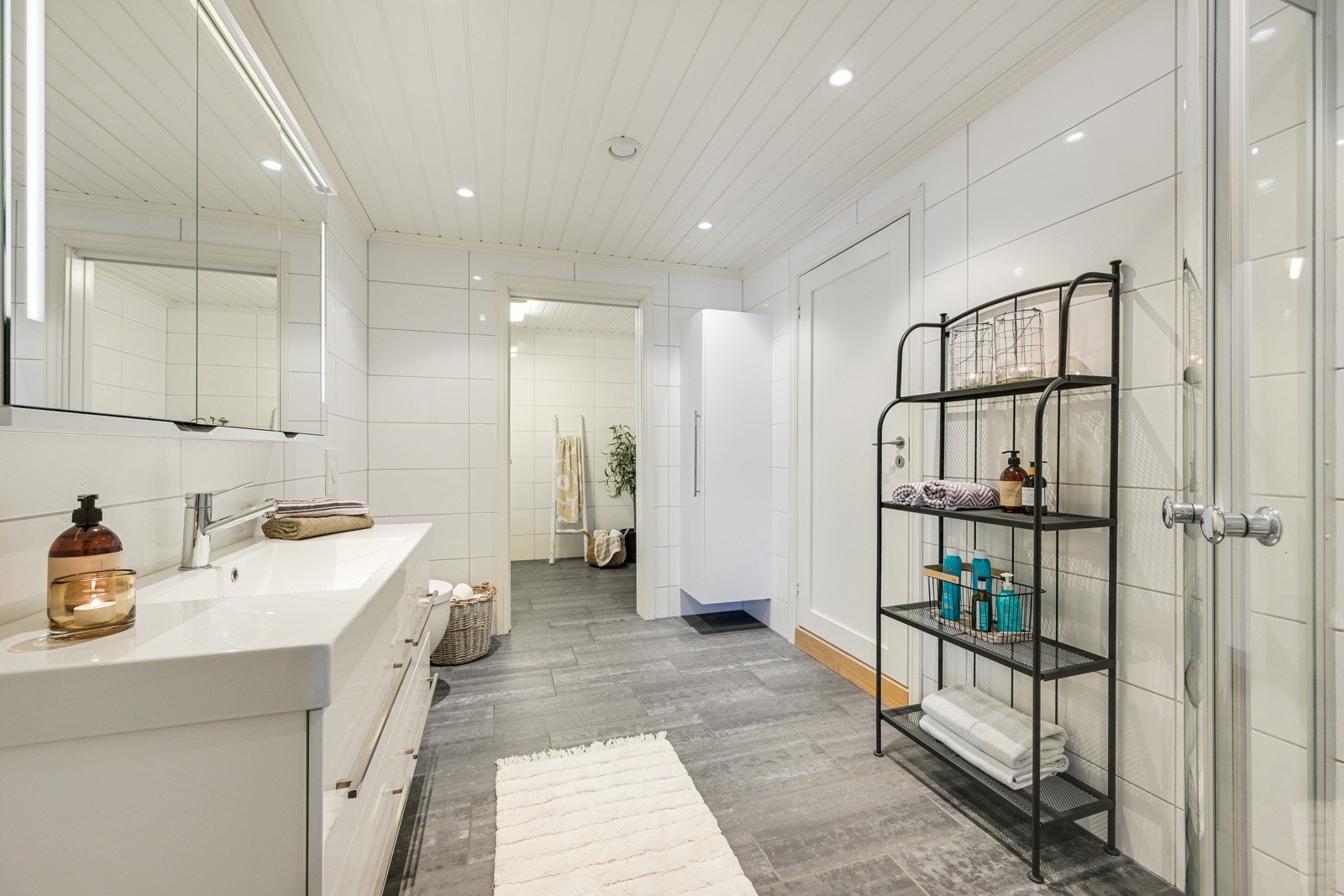 Badene er stilrent innredet med hvite veggfliser og store, mørke gulvfliser for en fin kontrast Galleribilde