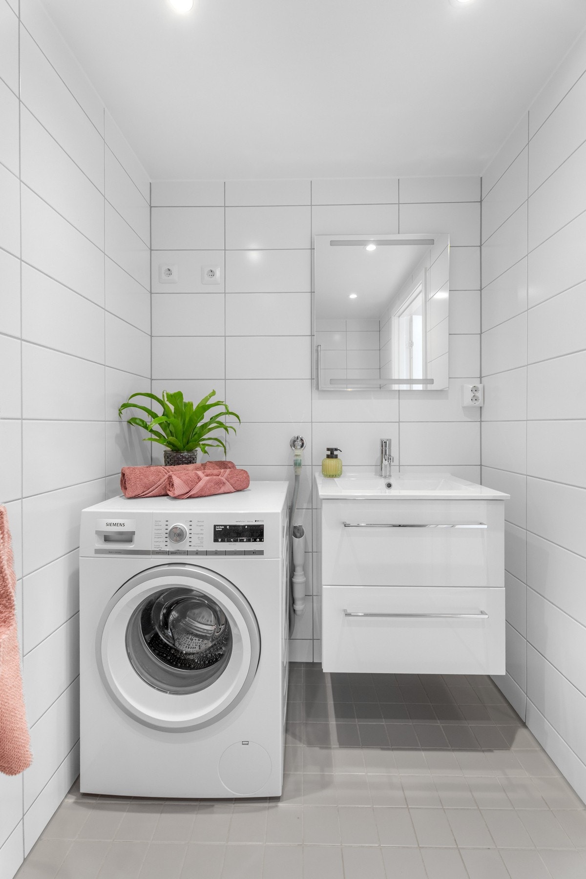 ervantinnredning med hvite høyglans fronter, hvit heldekkende servant, krom blandebatteri og moderne speil med innebygd lys på vegg. Galleribilde